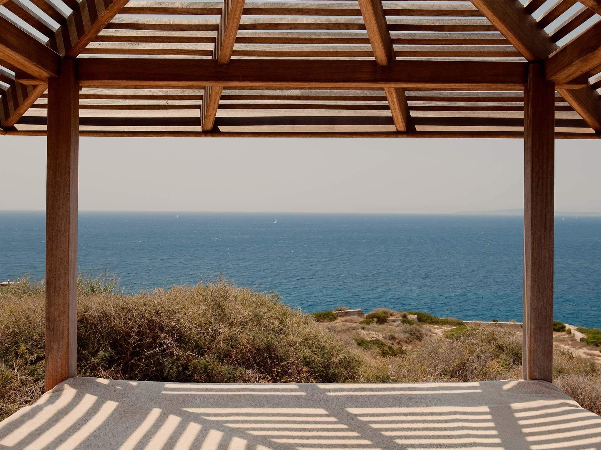 Cap Rocat: a bed with sheer cream curtains, wooden ceiling beams, and a window framing the sea