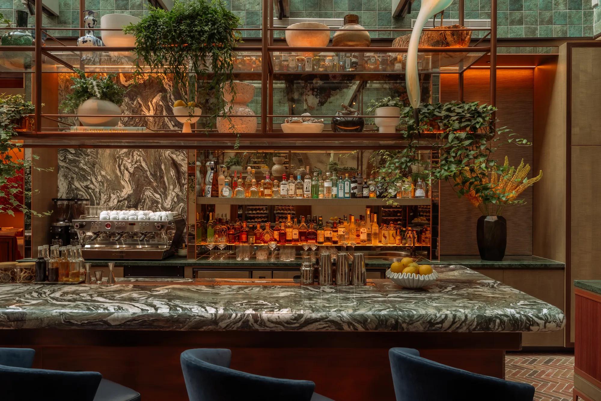 Rosewood Amsterdam: the bar at Eeuwen with a marble counter and shelves of plants and bottles