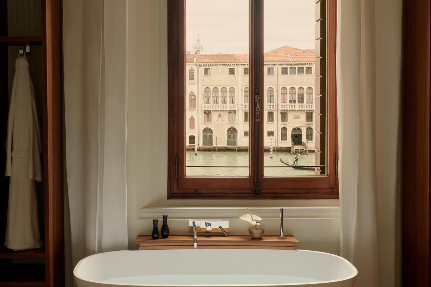 A soaking tub positioned at a tall window overlooking the Grand Canal with wooden trim framing the view