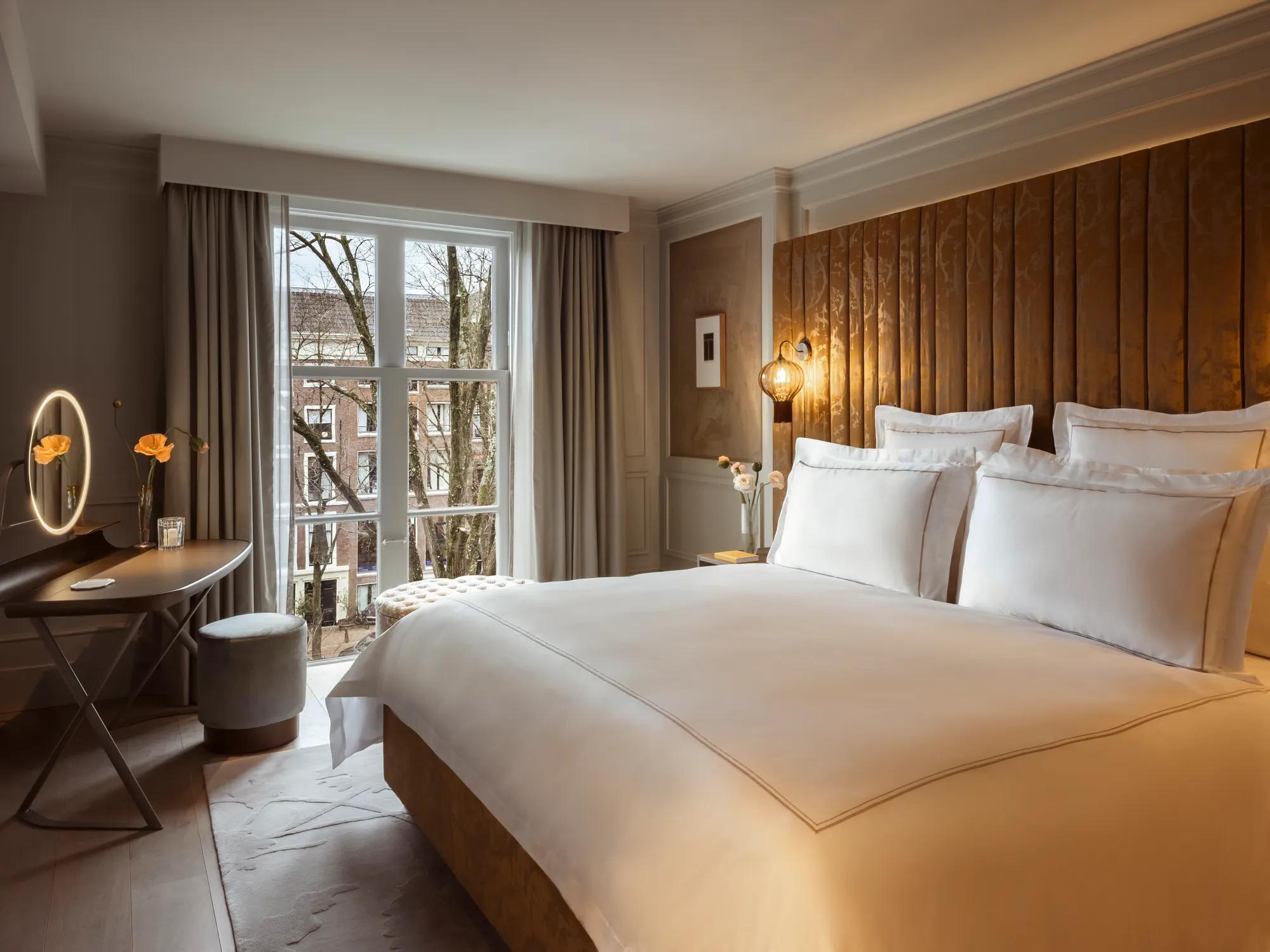 Rosewood Amsterdam: a Canal View Executive Suite bedroom with a wood headboard, a desk, and canal views
