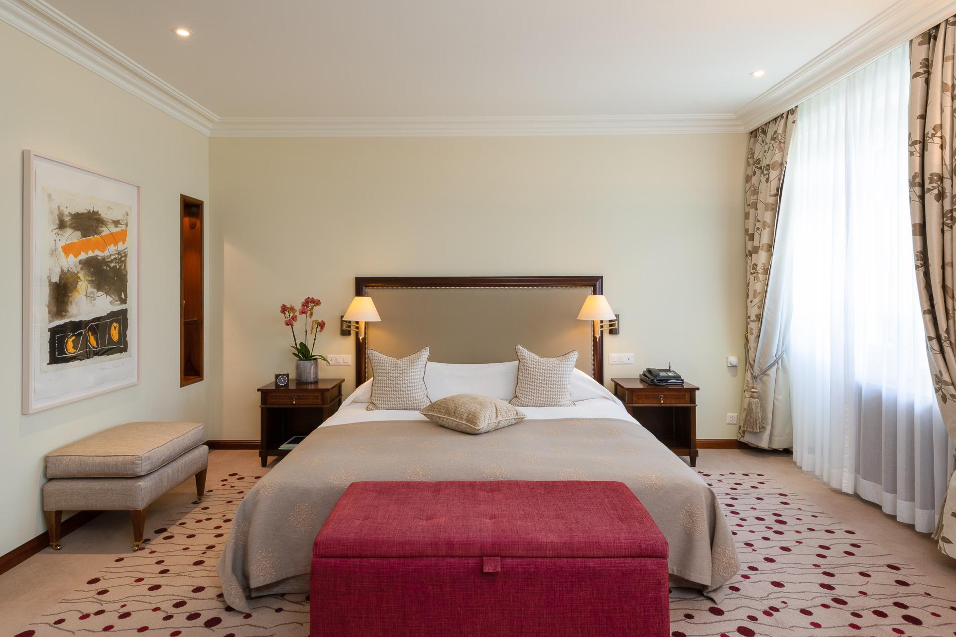 Suvretta House: a luxury bedroom with a king bed, warm wood tones, large windows, and classic alpine decor