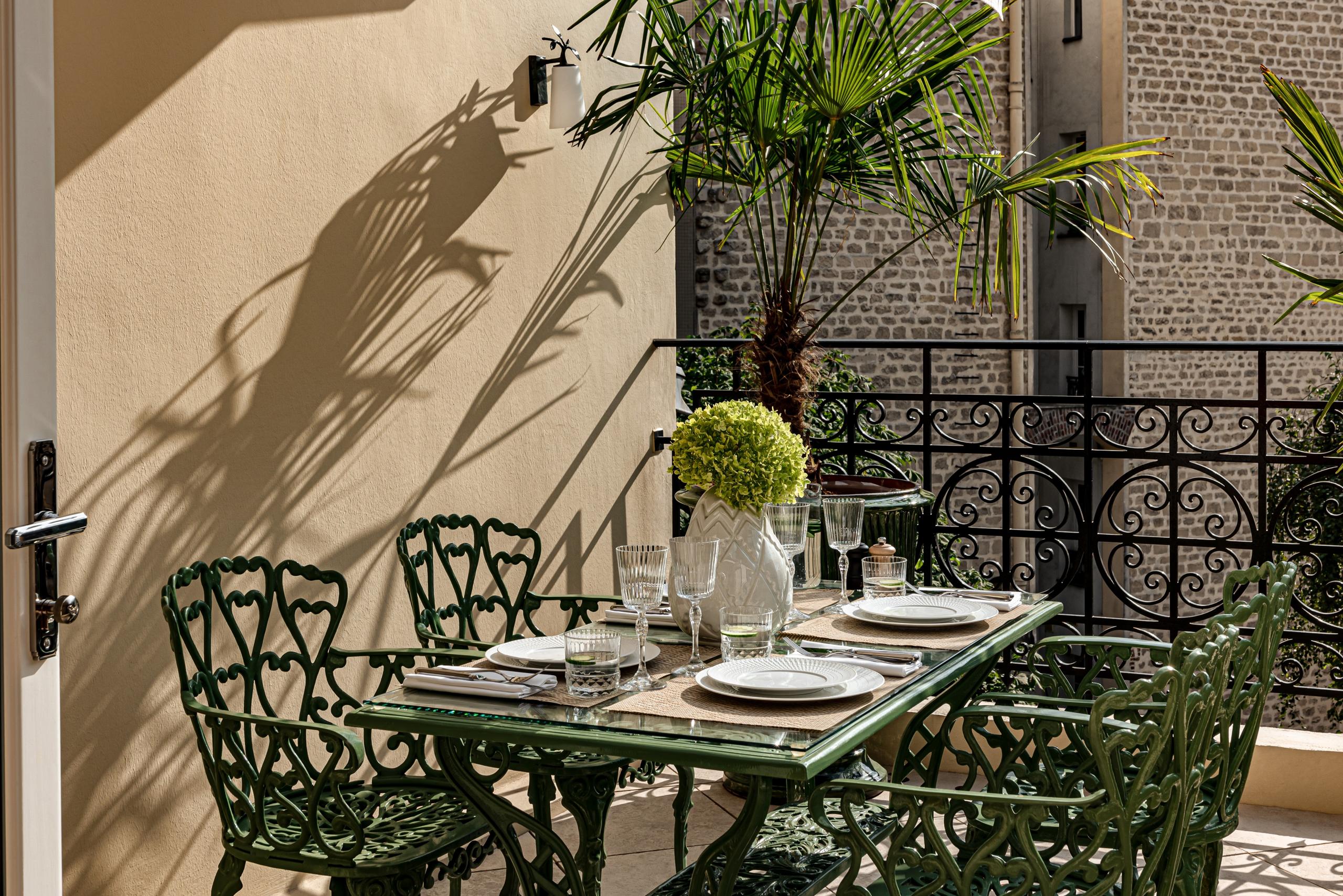 Saint James: wrought-iron bistro chairs on shaded garden patio, afternoon light casting shadows on stone