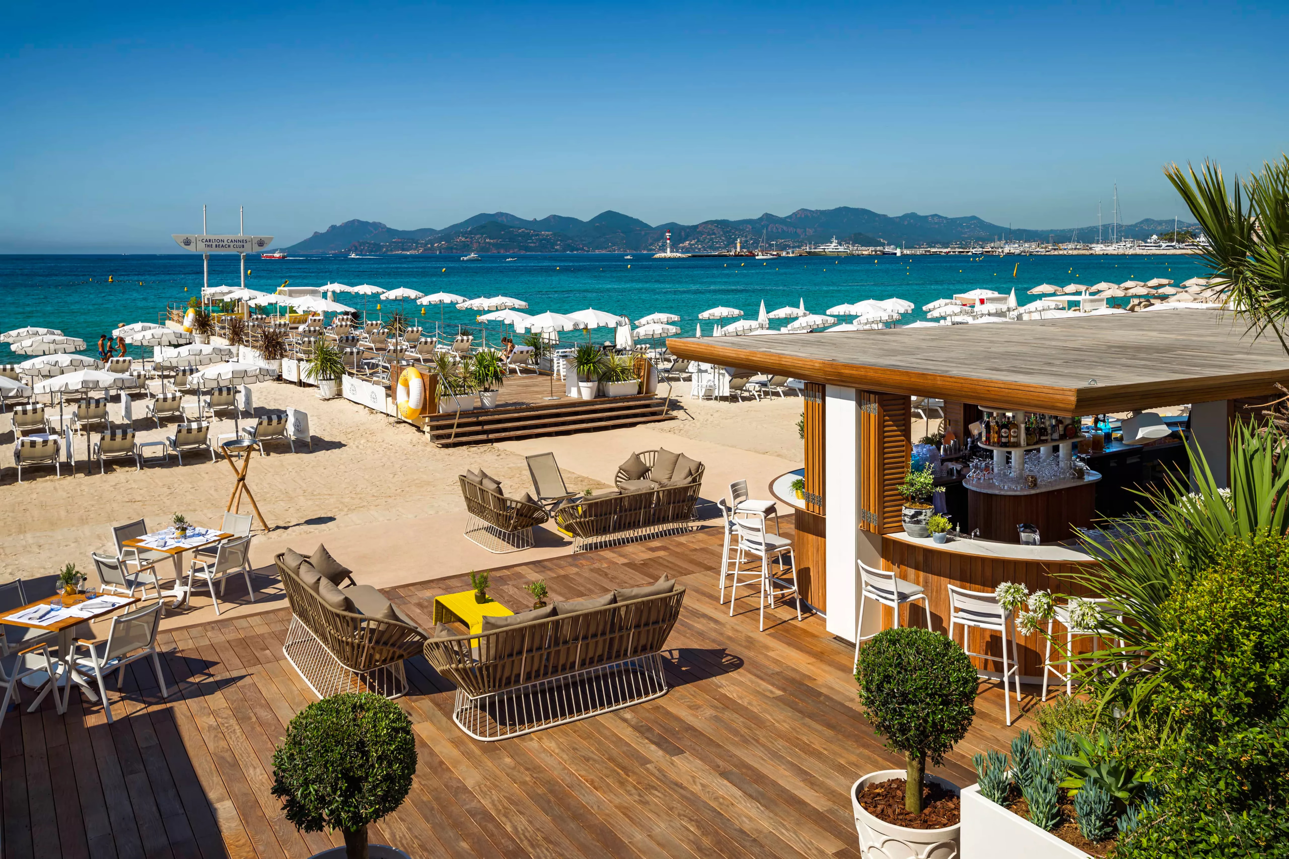 Carlton Cannes: beach club deck overlooking the Mediterranean with lounge beds and umbrellas in cream and blue tones
