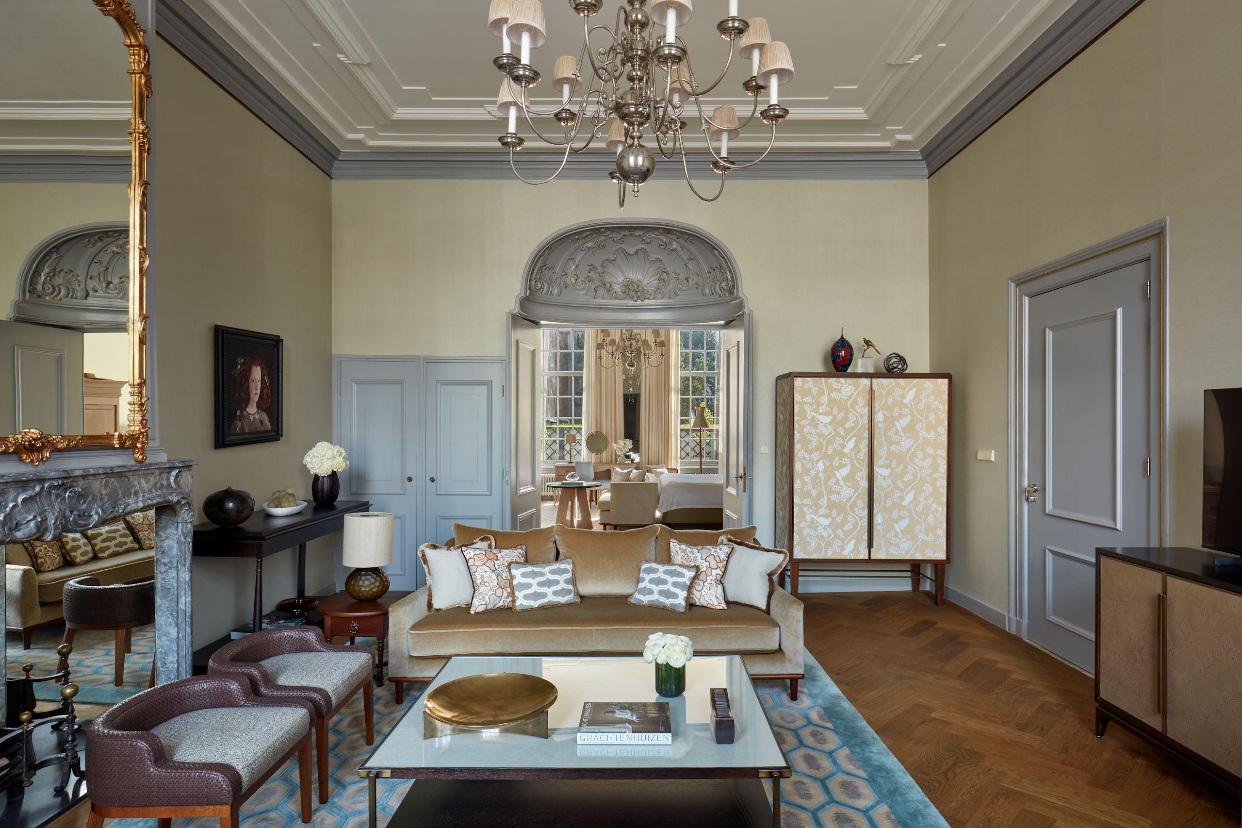 Waldorf Astoria Amsterdam: a formal sitting room with muted green walls, gold-framed artworks, and blue cushioned seating arranged around a marble fireplace