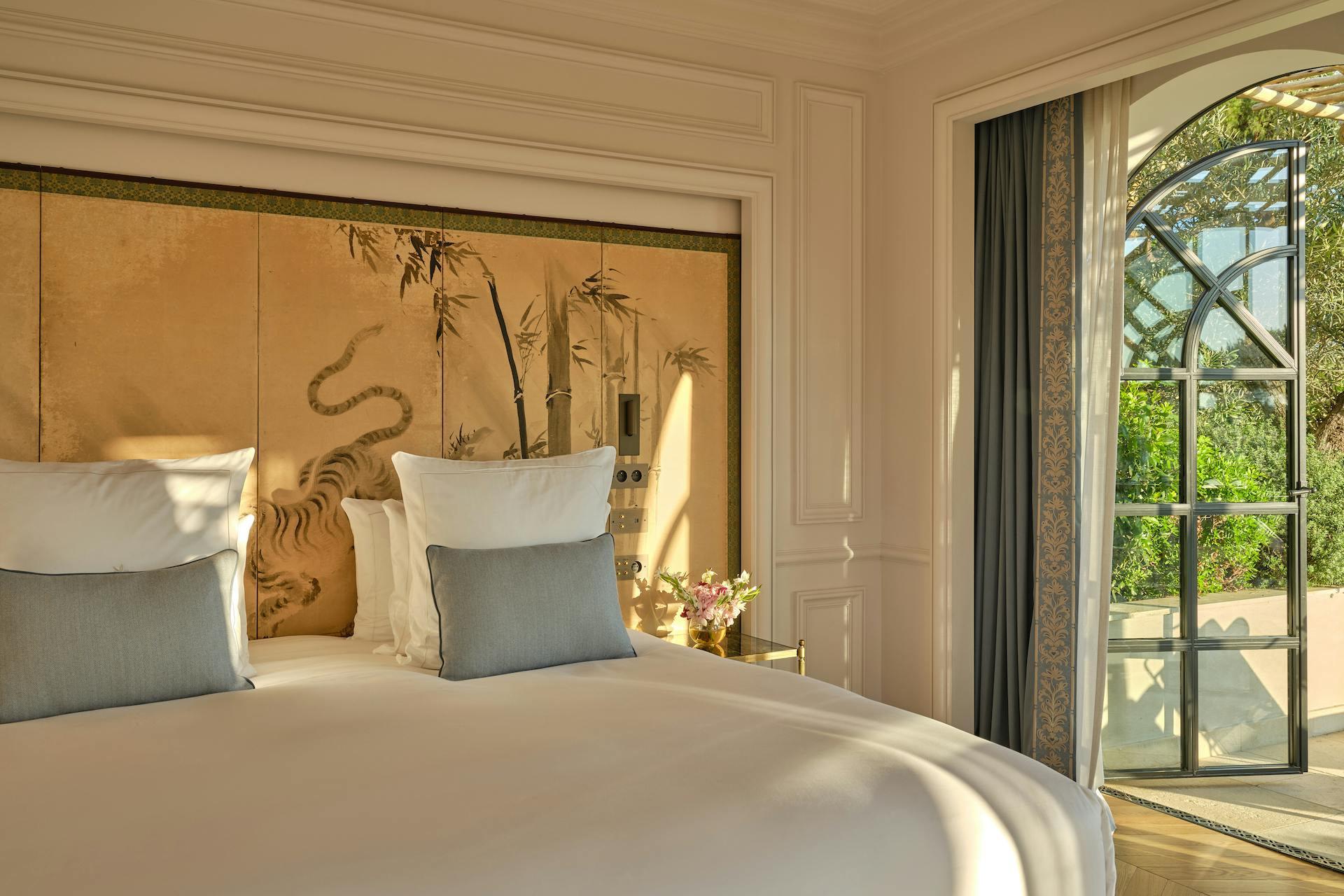 Château de La Messardière: bedroom with blue accent pillows, wooden finishes, and large glass doors to gardens