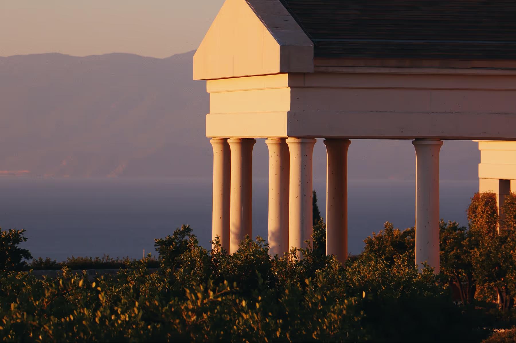 Amanzoe: illuminated columnwork with mountains and water at twilight