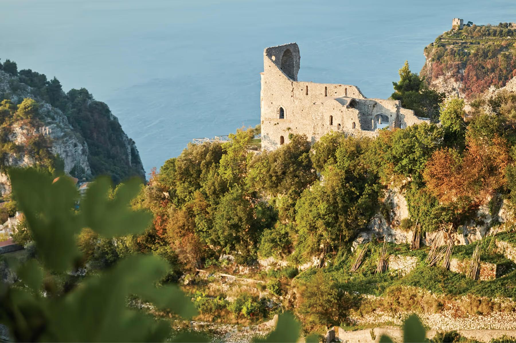 Caruso: medieval hilltop tower ruins surrounded by vegetation with sea and landscape beyond