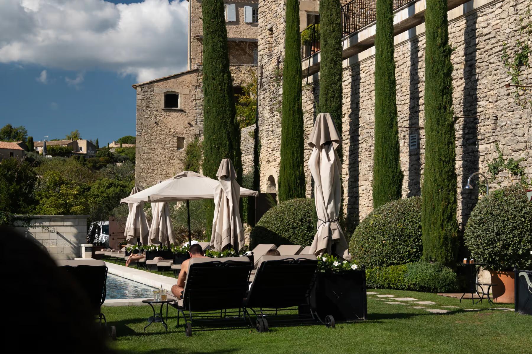 Airelles Gordes, La Bastide: manicured lawn with stone walls, shaded pavilion, and distant valley views