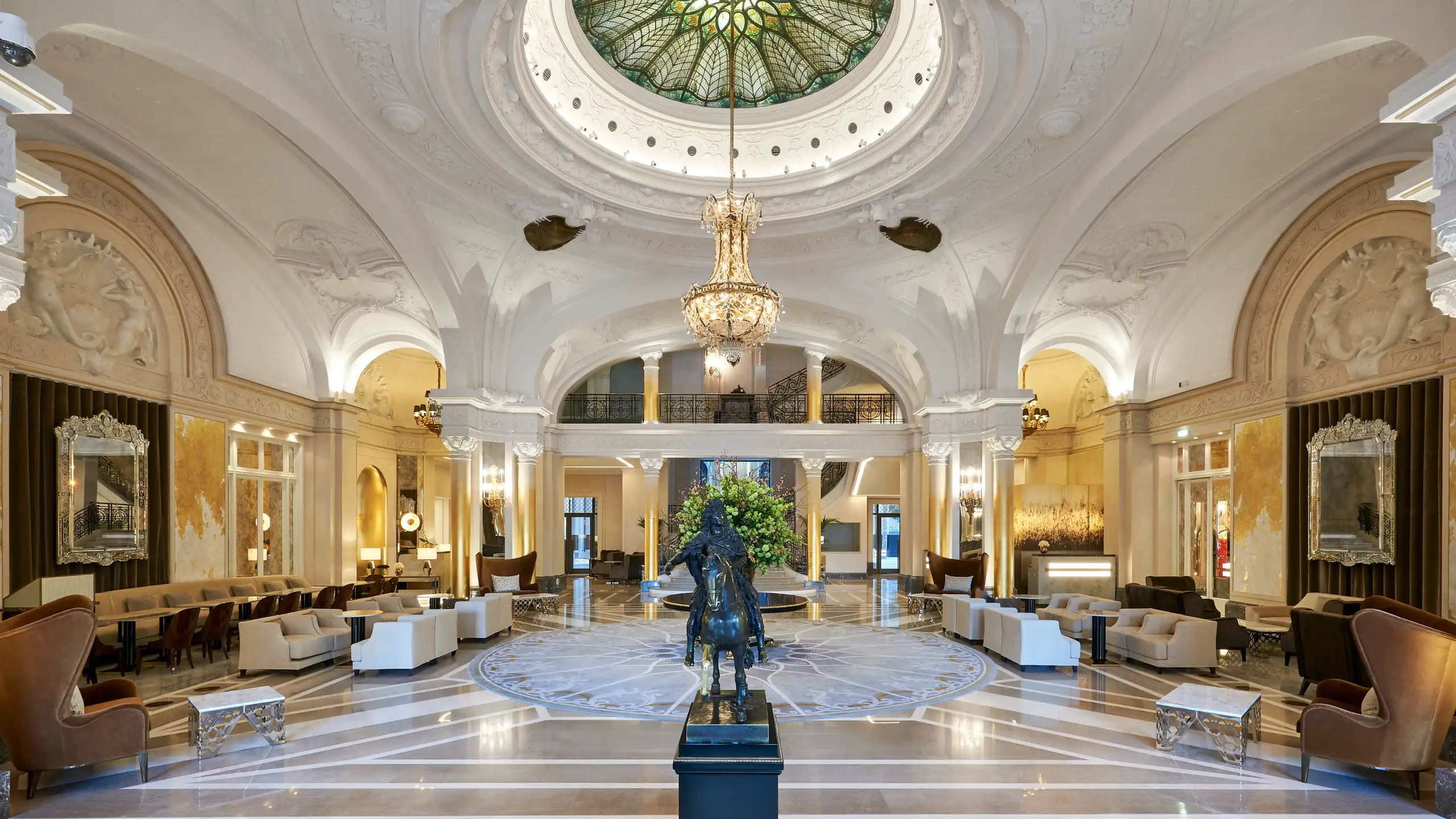 Grand lobby with painted ceiling dome, marble floors, gilt arches, and skylight