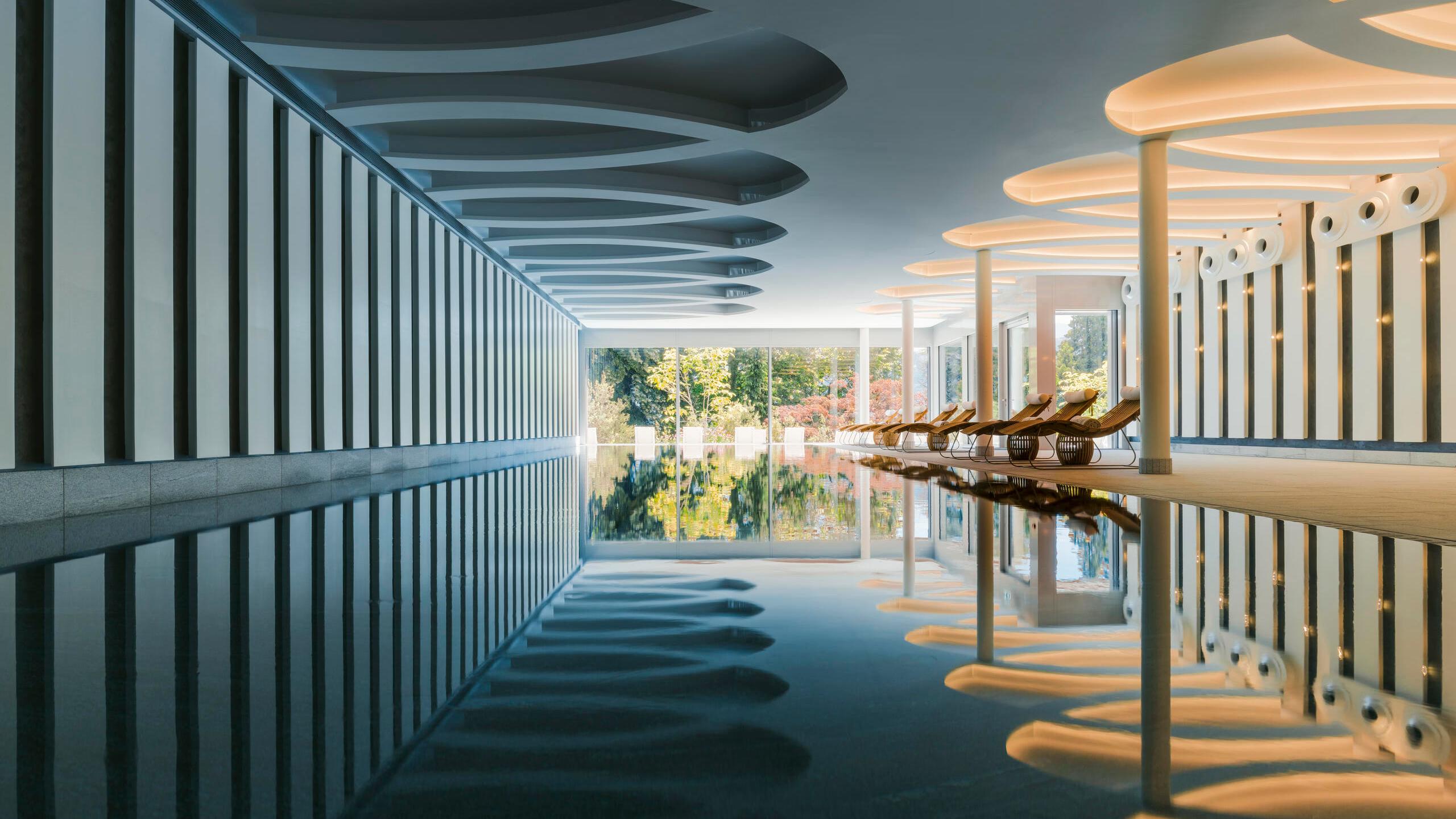A spa corridor with dark blue carpeting and striped white-and-teal ceiling dividers, facing lake-view windows