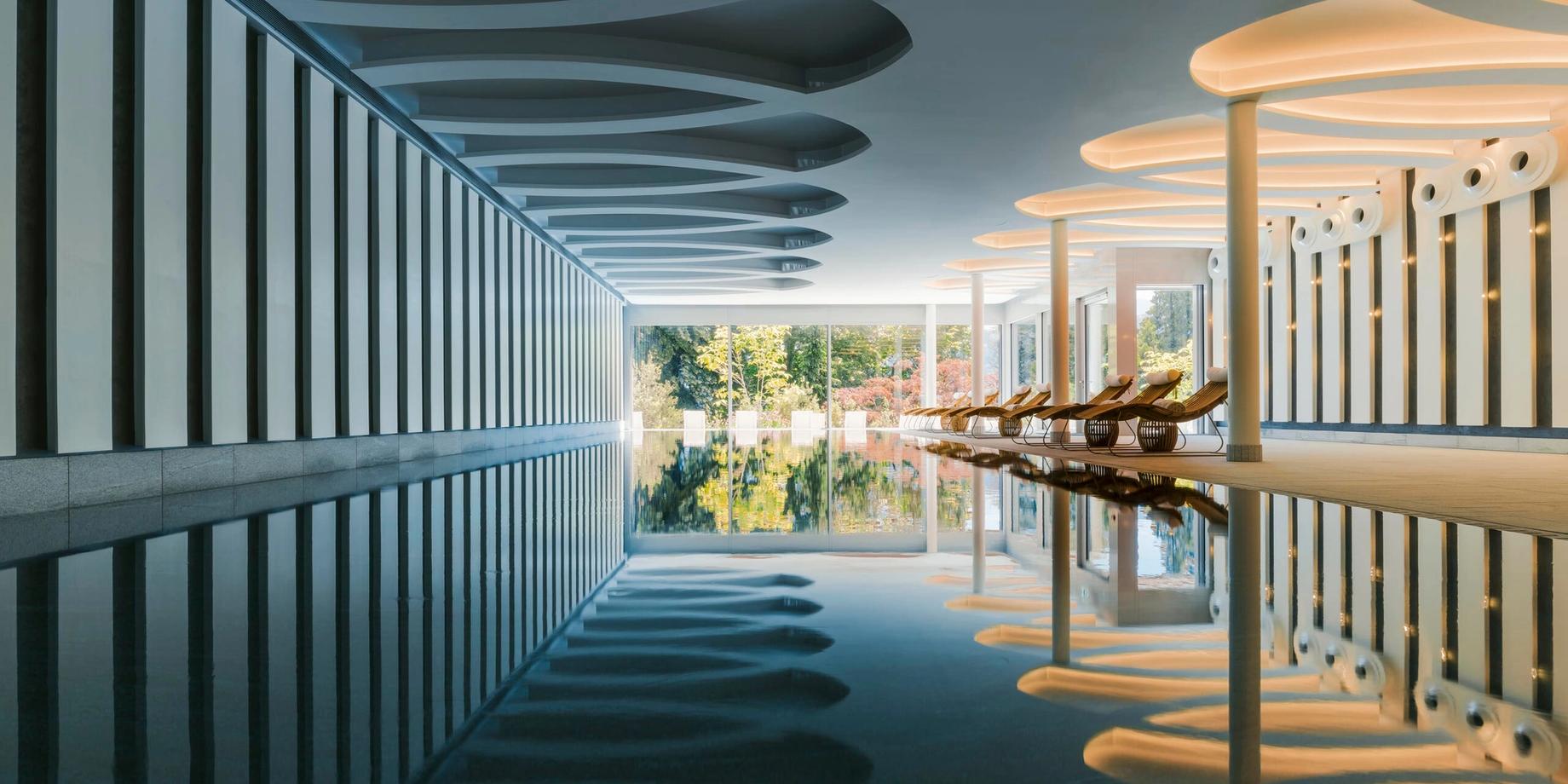 A spa corridor with dark blue carpeting and striped white-and-teal ceiling dividers, facing lake-view windows
