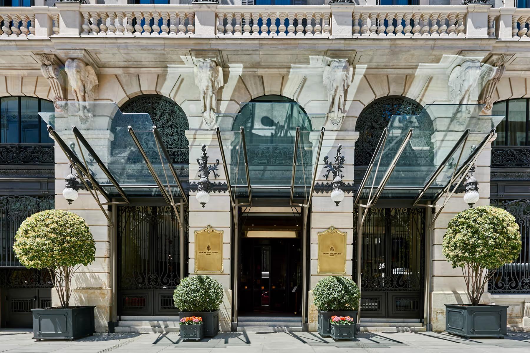 Four Seasons Hotel Madrid: black and glass entry doors with limestone archway and marble facade, flanked by topiary plantings