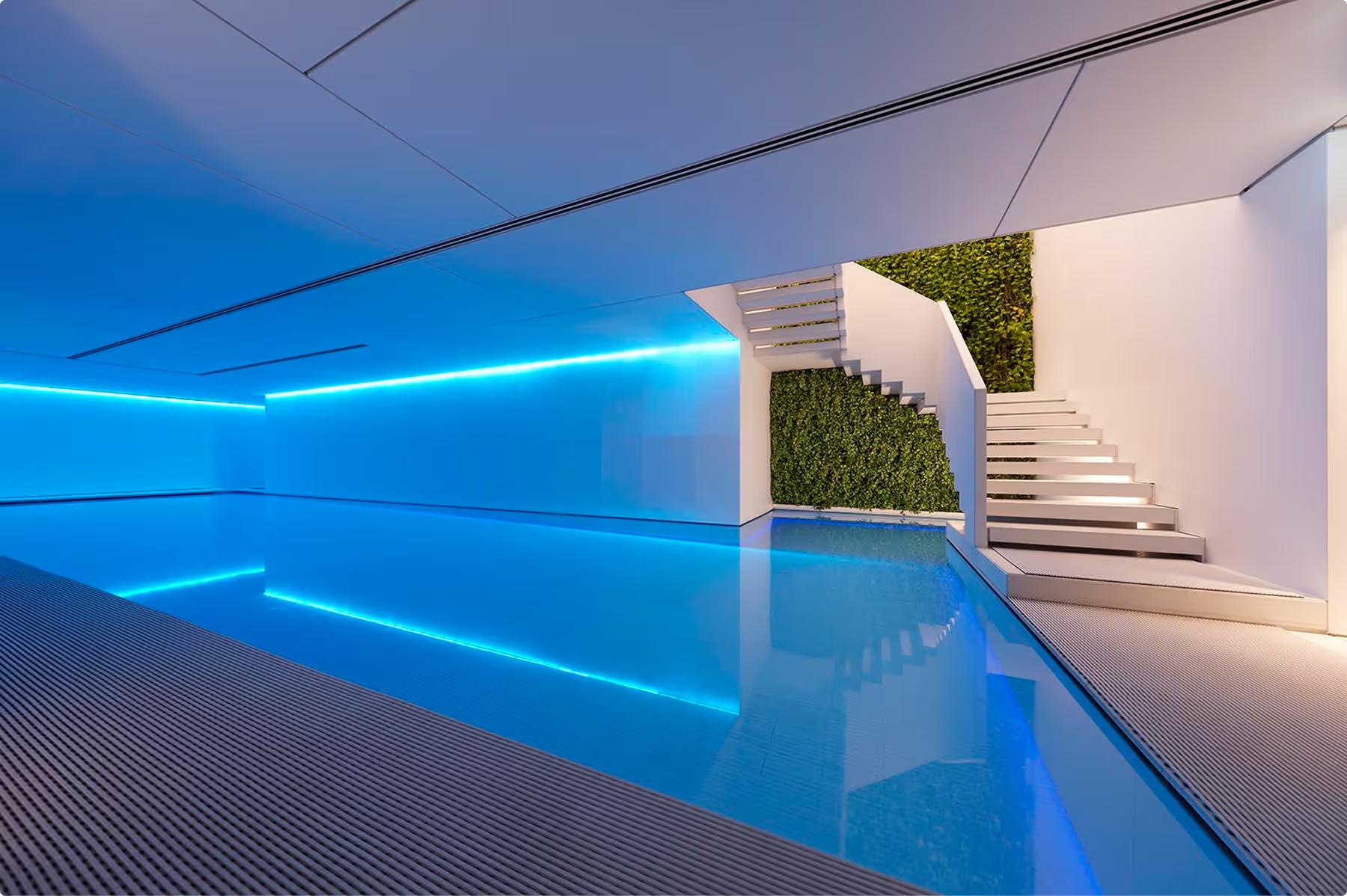Mandarin Oriental Conservatorium, Amsterdam: indoor pool in blue light, with a white staircase and a green plant wall at the far end