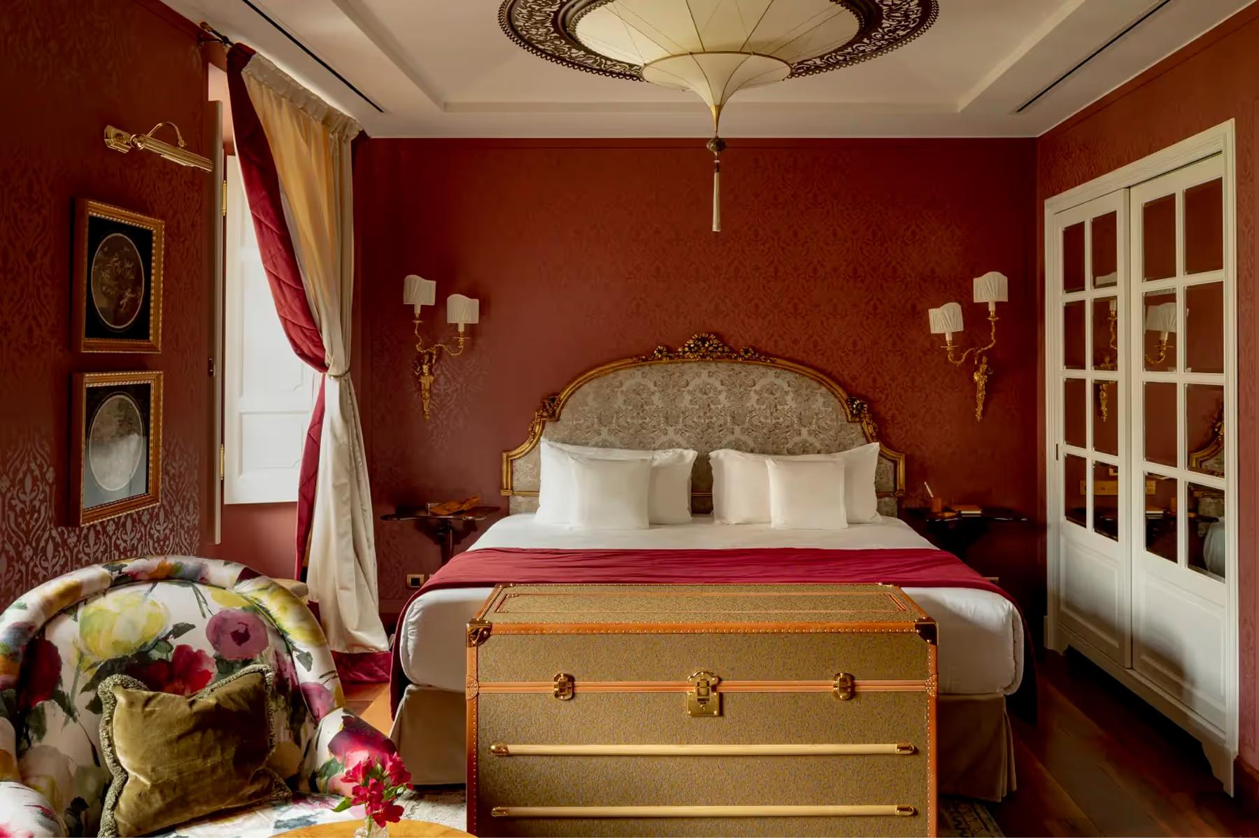 Passalacqua: a bedroom with deep red walls, gilded bed, and tall white doors opening to windows