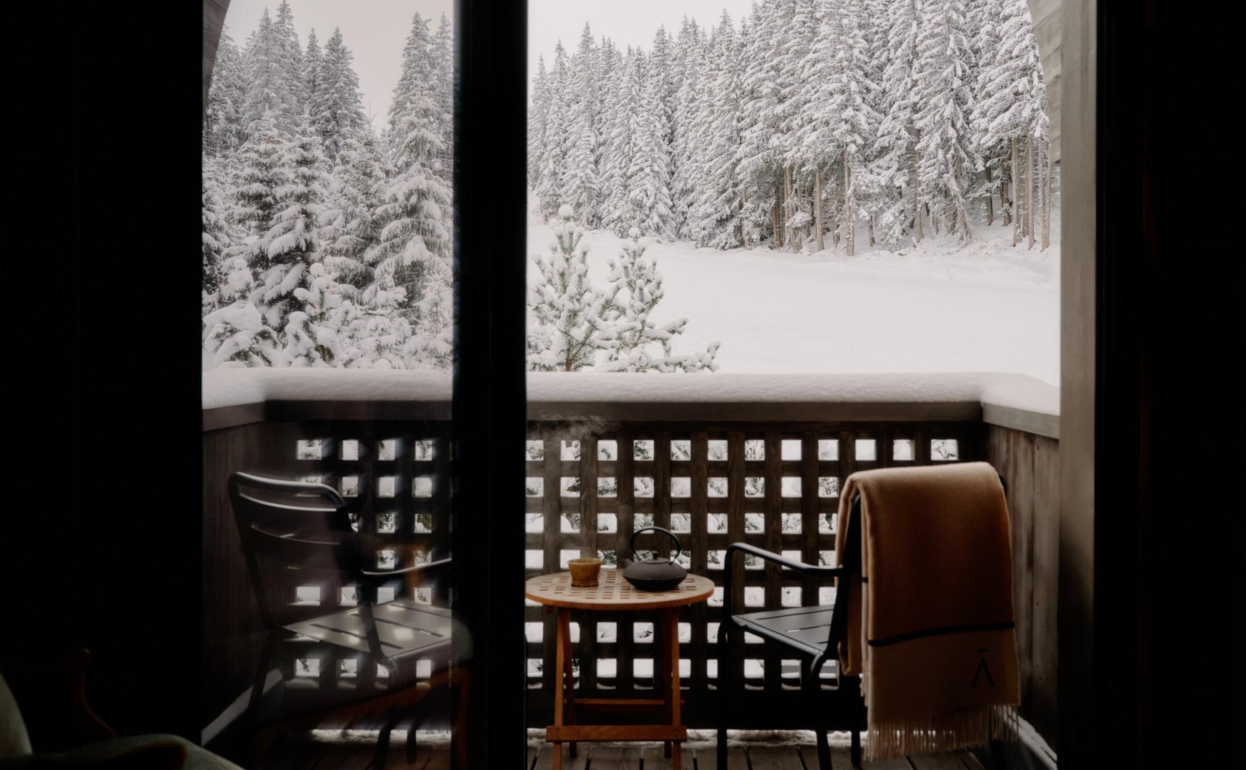 Aman Le Mélézin: private balcony with armchairs, a side table, and a wool blanket overlooking snow laden pines