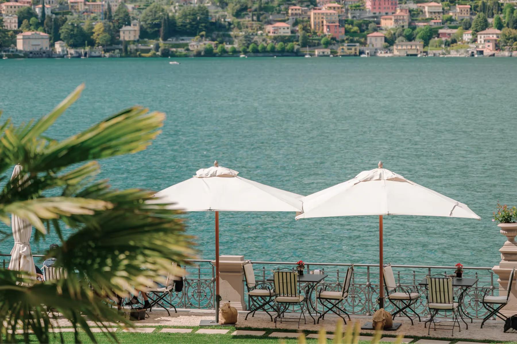 Waterfront dining with white umbrellas, wooden chairs, and turquoise lake water