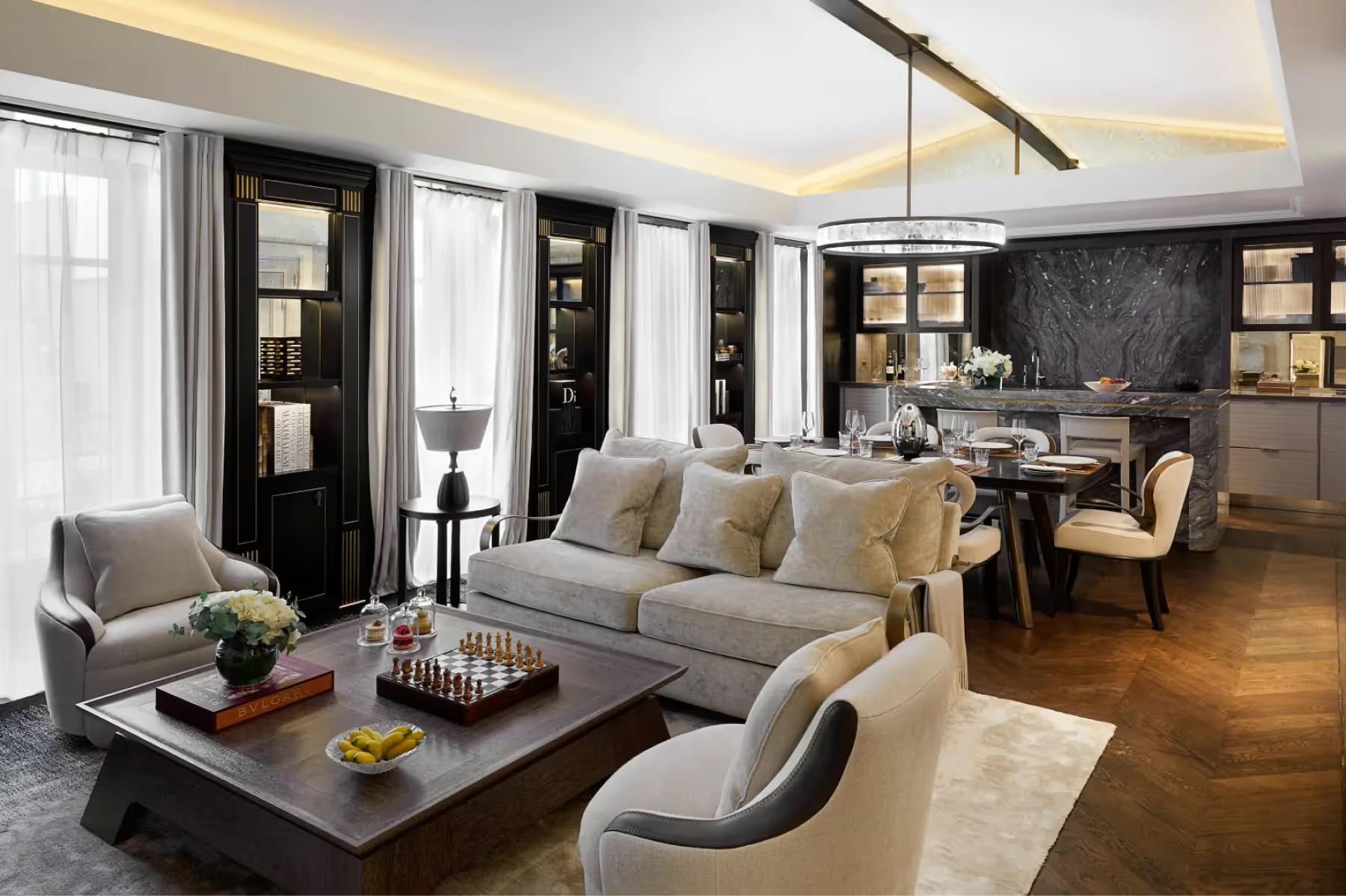 Maison Villeroy: a suite living area with gray sofa, dark coffee table, and pale armchairs near bright windows
