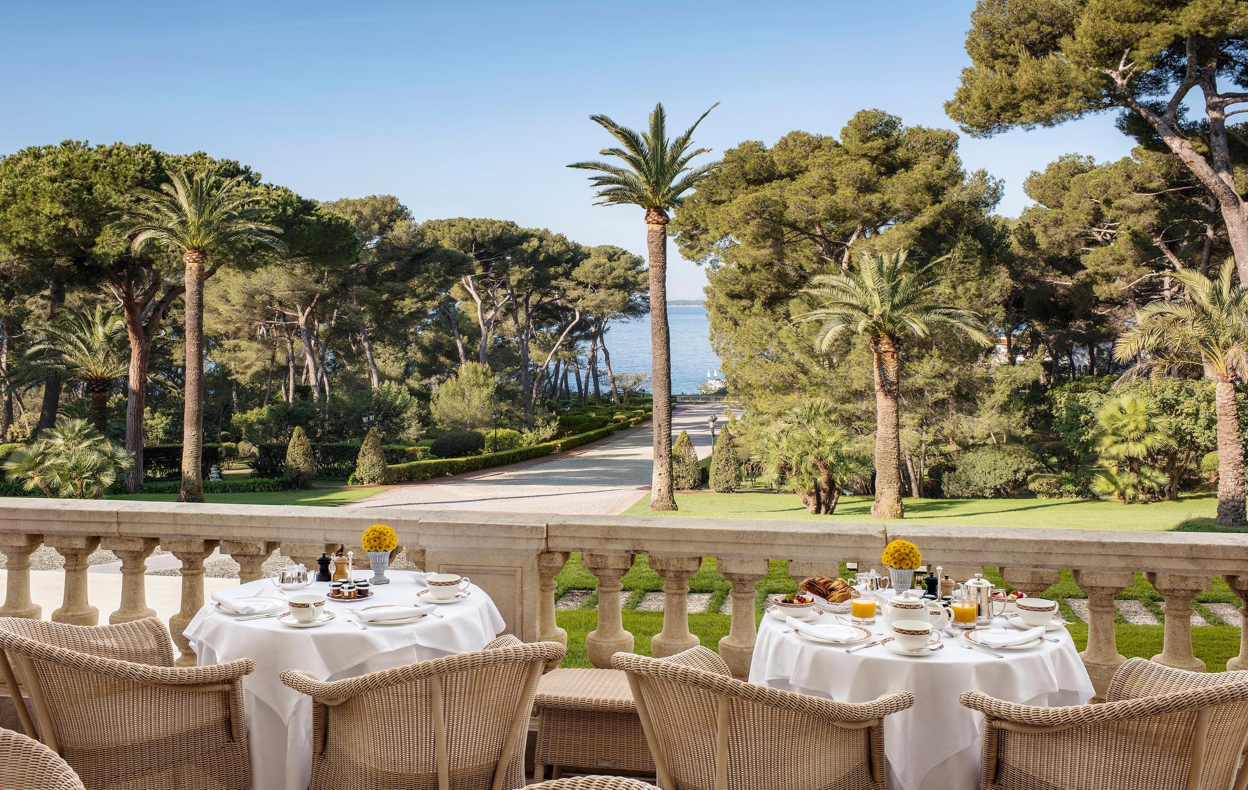 Hôtel du Cap-Eden-Roc: an outdoor dining table set on a terrace with palm trees and sea views beyond manicured lawns