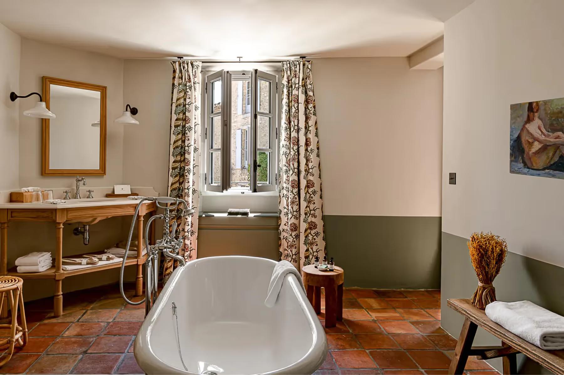 Hôtel Crillon le Brave: a white freestanding bathtub in a stone bathroom with half-painted green walls and wooden furniture