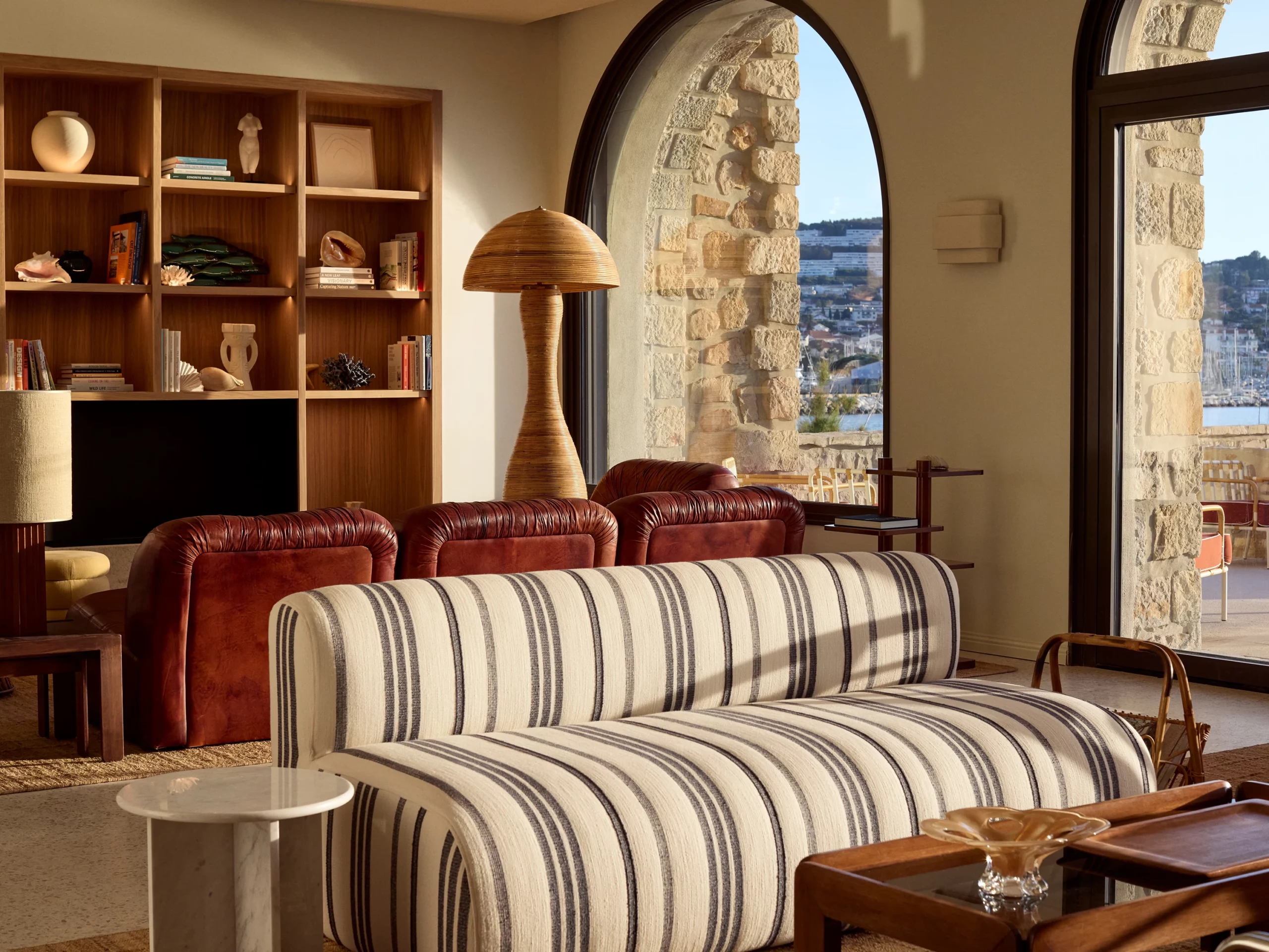 Cognac leather armchairs and a striped sofa face arched windows over the harbor