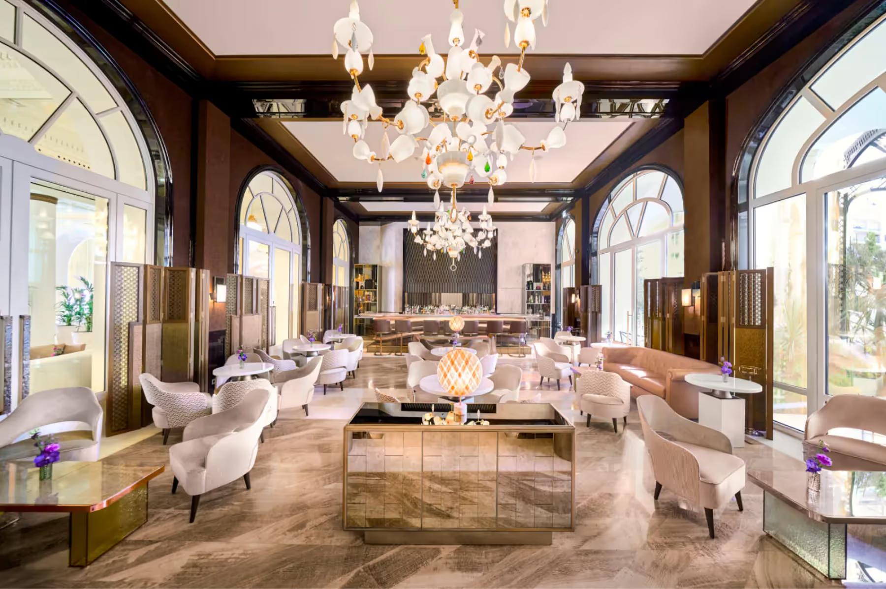 Carlton Cannes: elegant reception area with dark wood paneling, mirrors, white seating, and crystal chandelier overhead