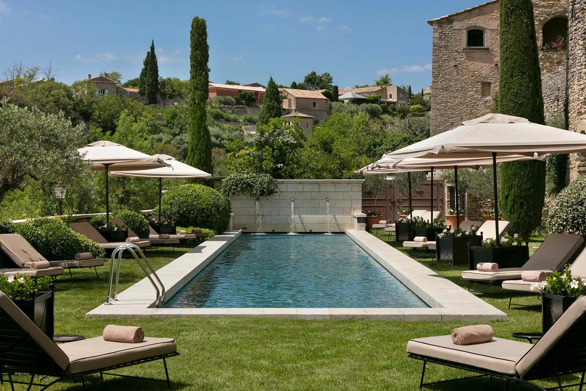 Airelles Gordes, La Bastide: rectangular pool lined with loungers and white umbrellas surrounded by stone walls and cypress