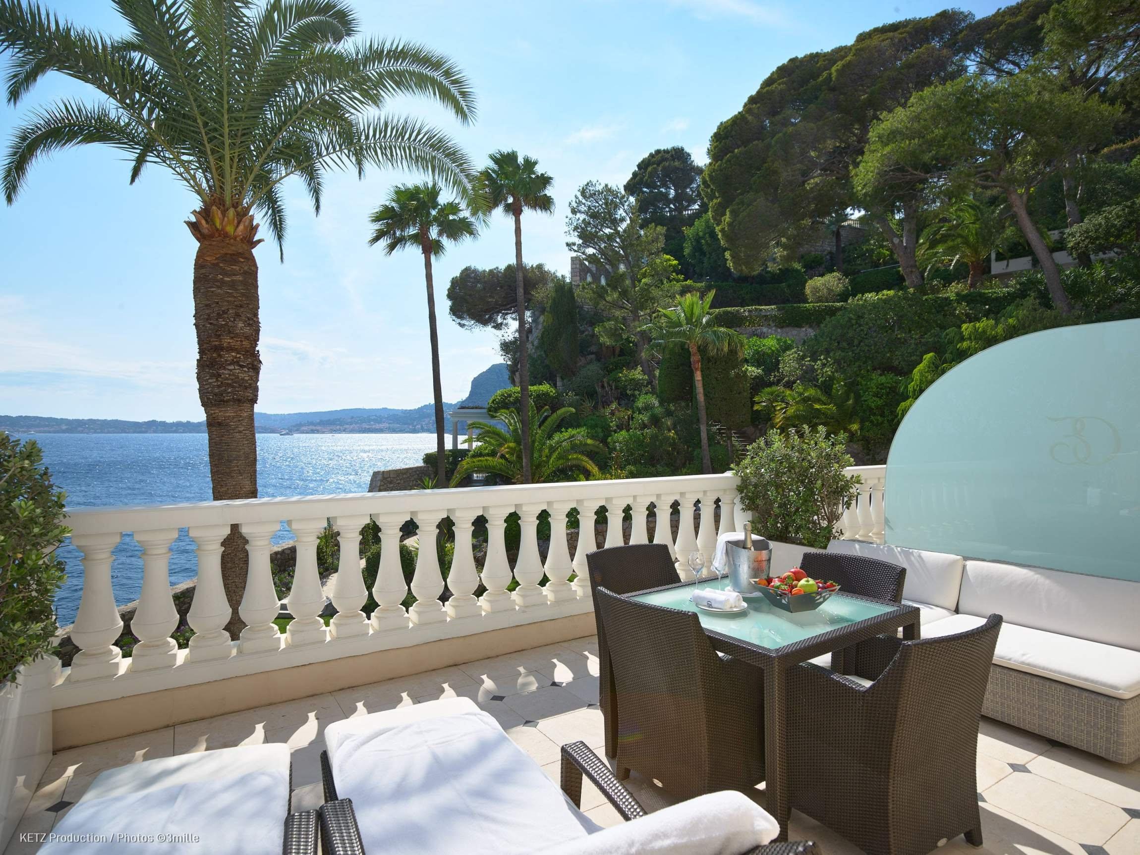 Hotel Cap-Estel: palm trees frame a stone terrace with seating and views across the Mediterranean