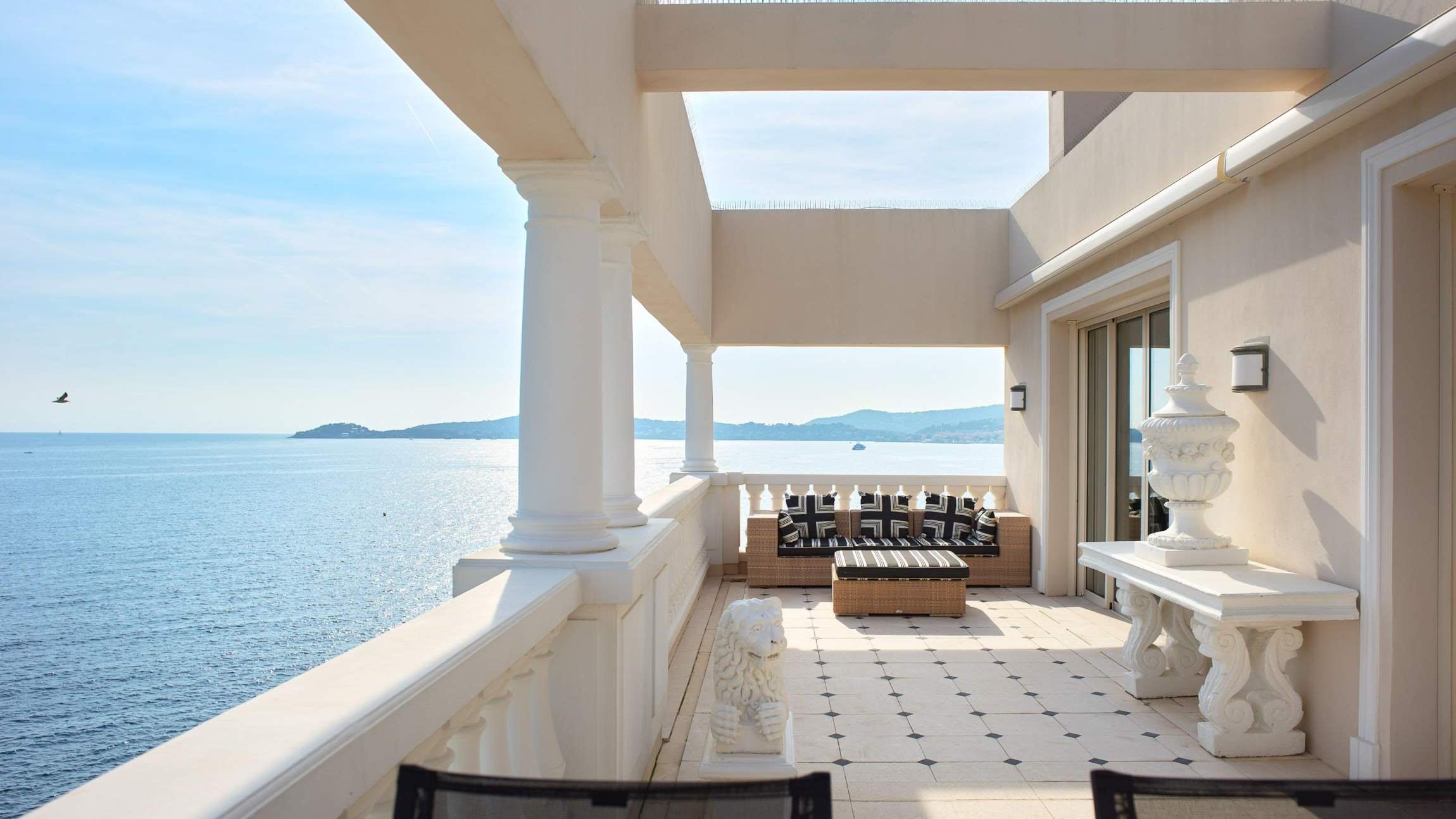 A modernist terrace with white columns overlooks calm Mediterranean waters