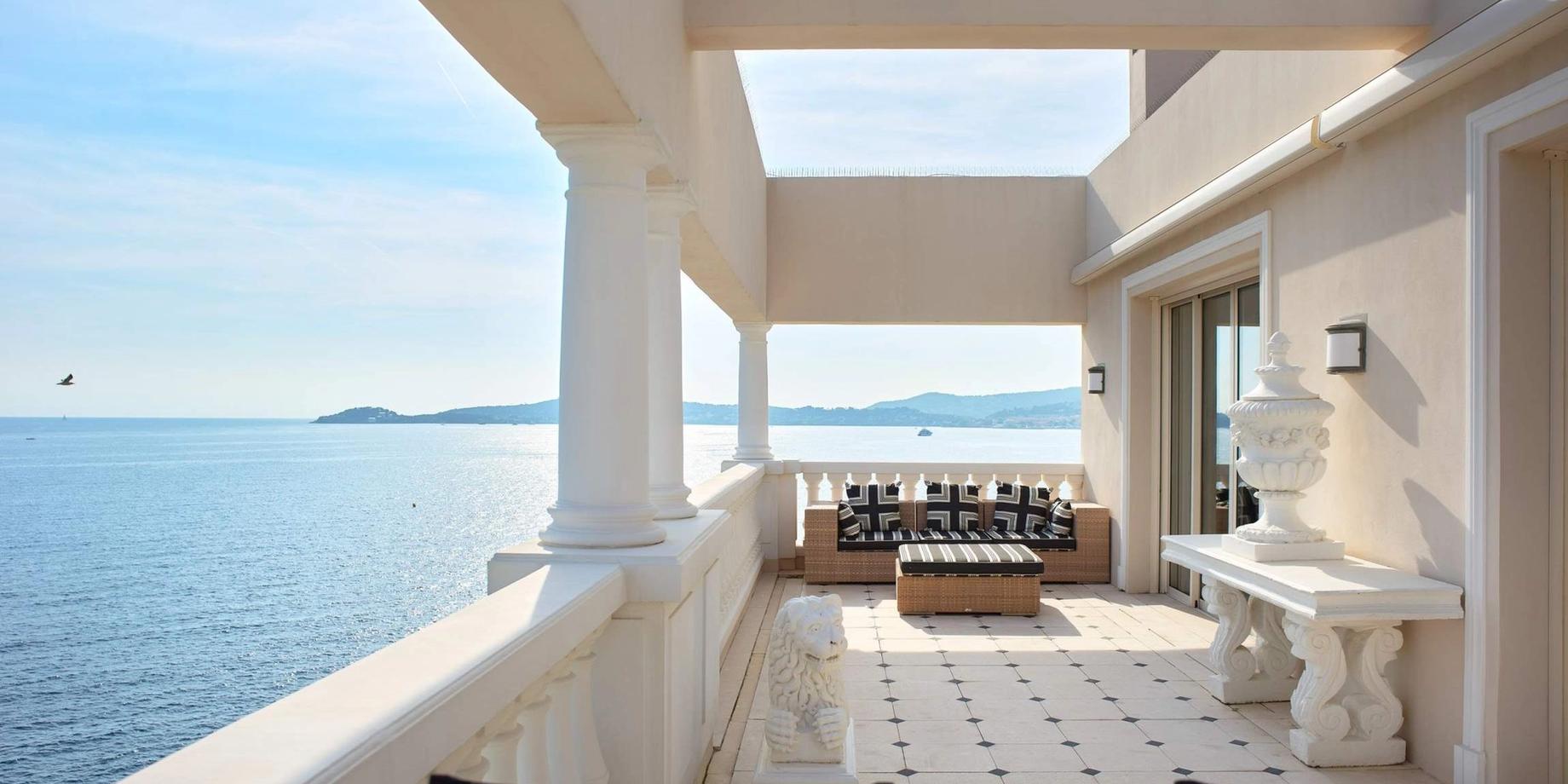 A modernist terrace with white columns overlooks calm Mediterranean waters