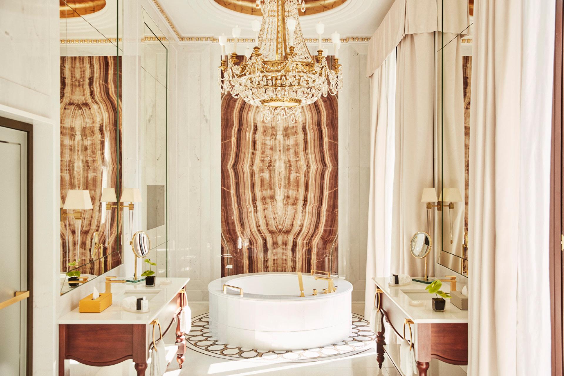 Spa bathroom with crystal chandelier, marble tub surround, brass fixtures, and ornate gold accents