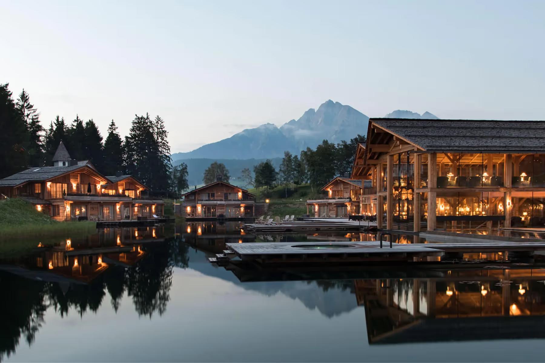 San Luis Retreat: the hotel lit at dusk beside a reflective lake with mountains behind