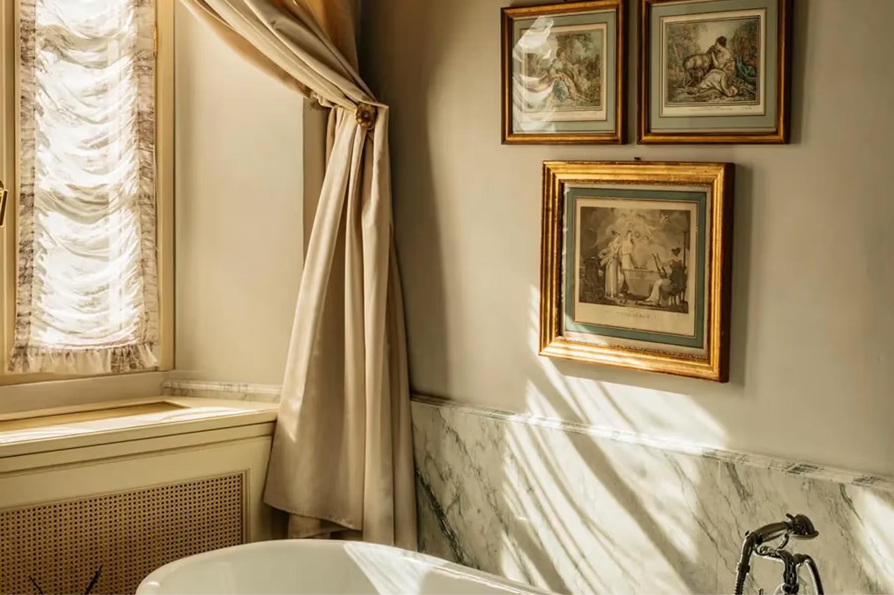 Passalacqua: a sun-filled bedroom corner with framed artwork, window, and cream bedding
