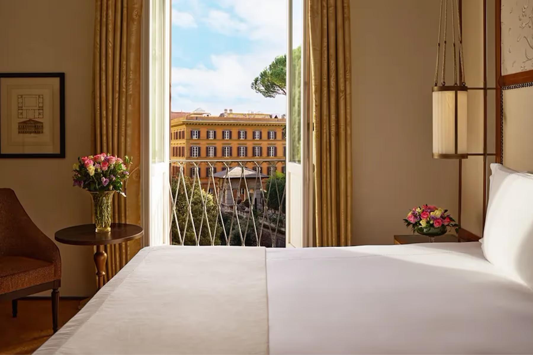 Hotel Eden: a bedroom window framing a view of a Rome palazzo’s dome and roofscape, with white bedding in the foreground