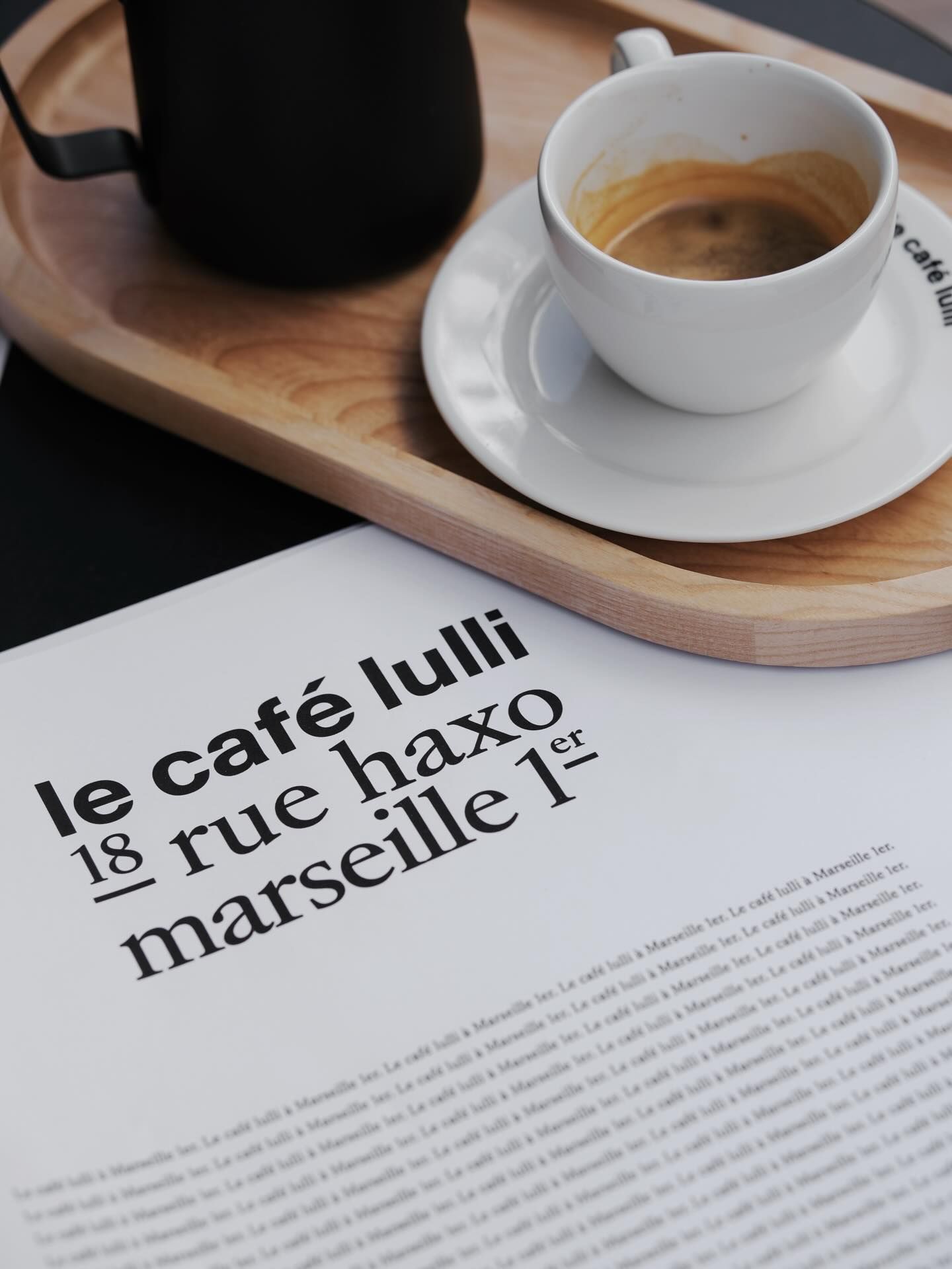 An espresso on a wooden tray beside a printed card for Le Café Lulli, 18 Rue Haxo