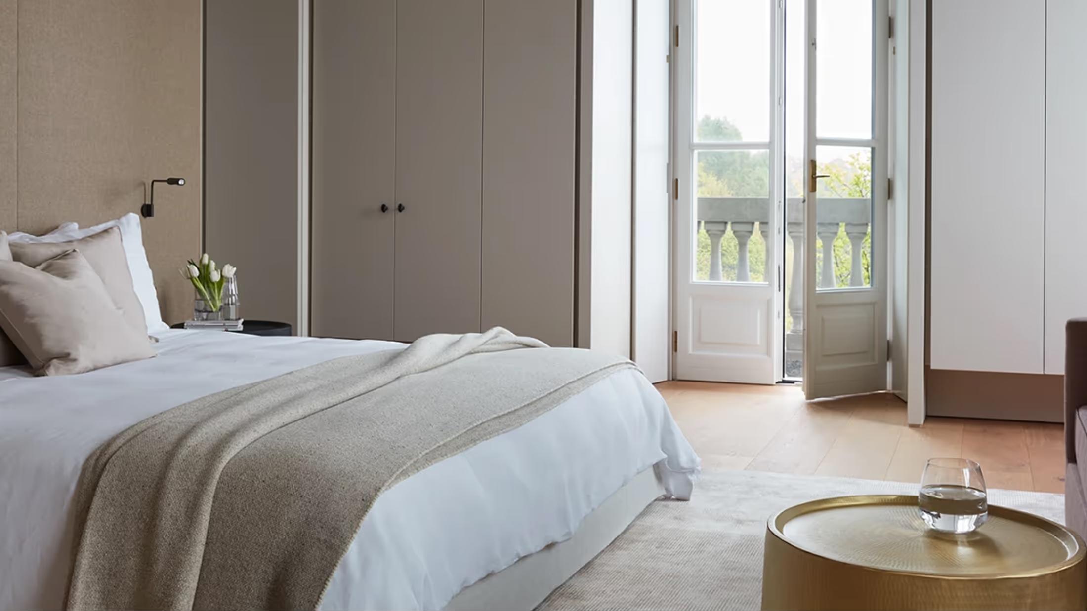 A bedroom with white bedding overlooking mountain peaks through wide terrace doors
