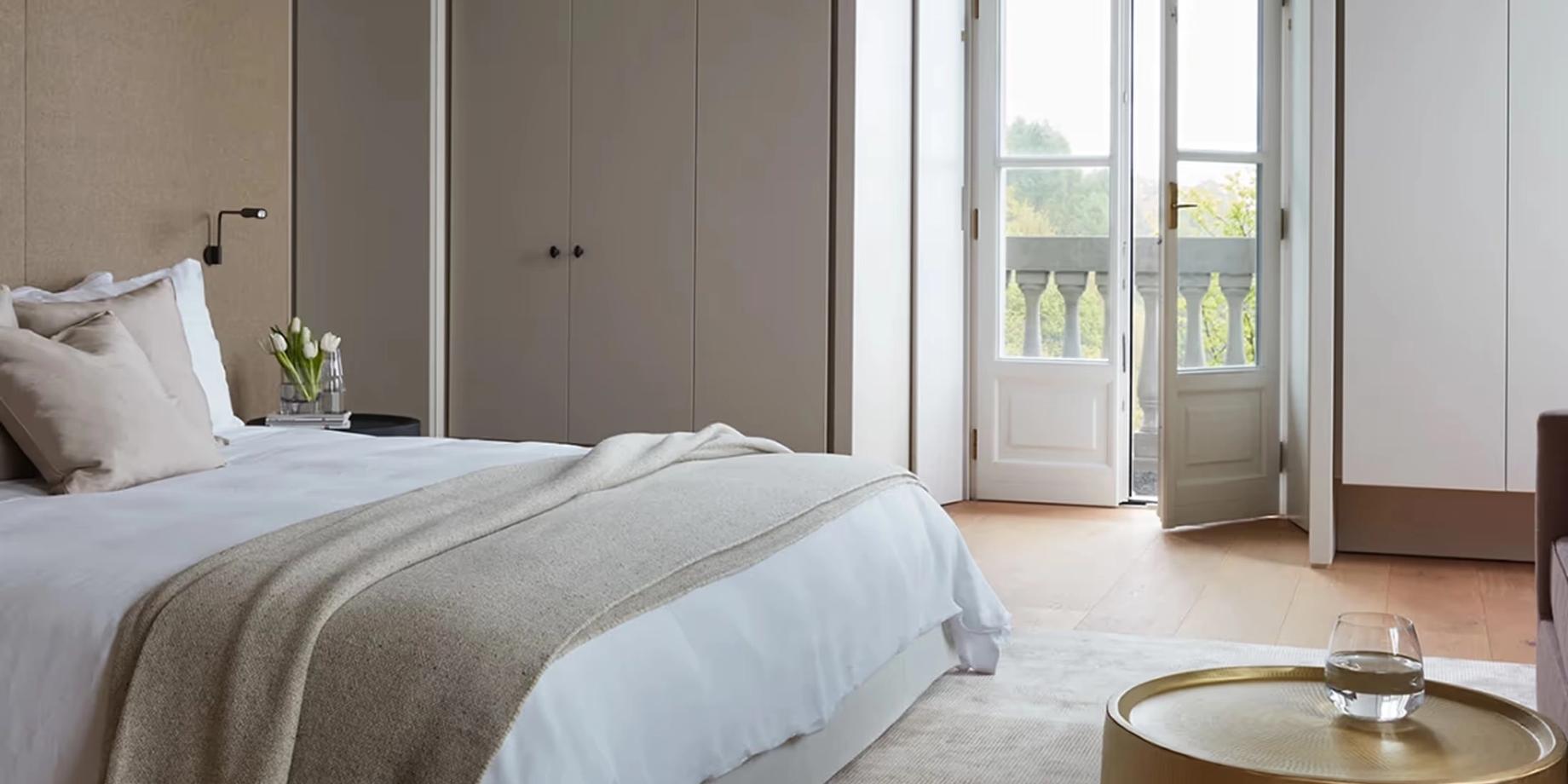 A bedroom with white bedding overlooking mountain peaks through wide terrace doors