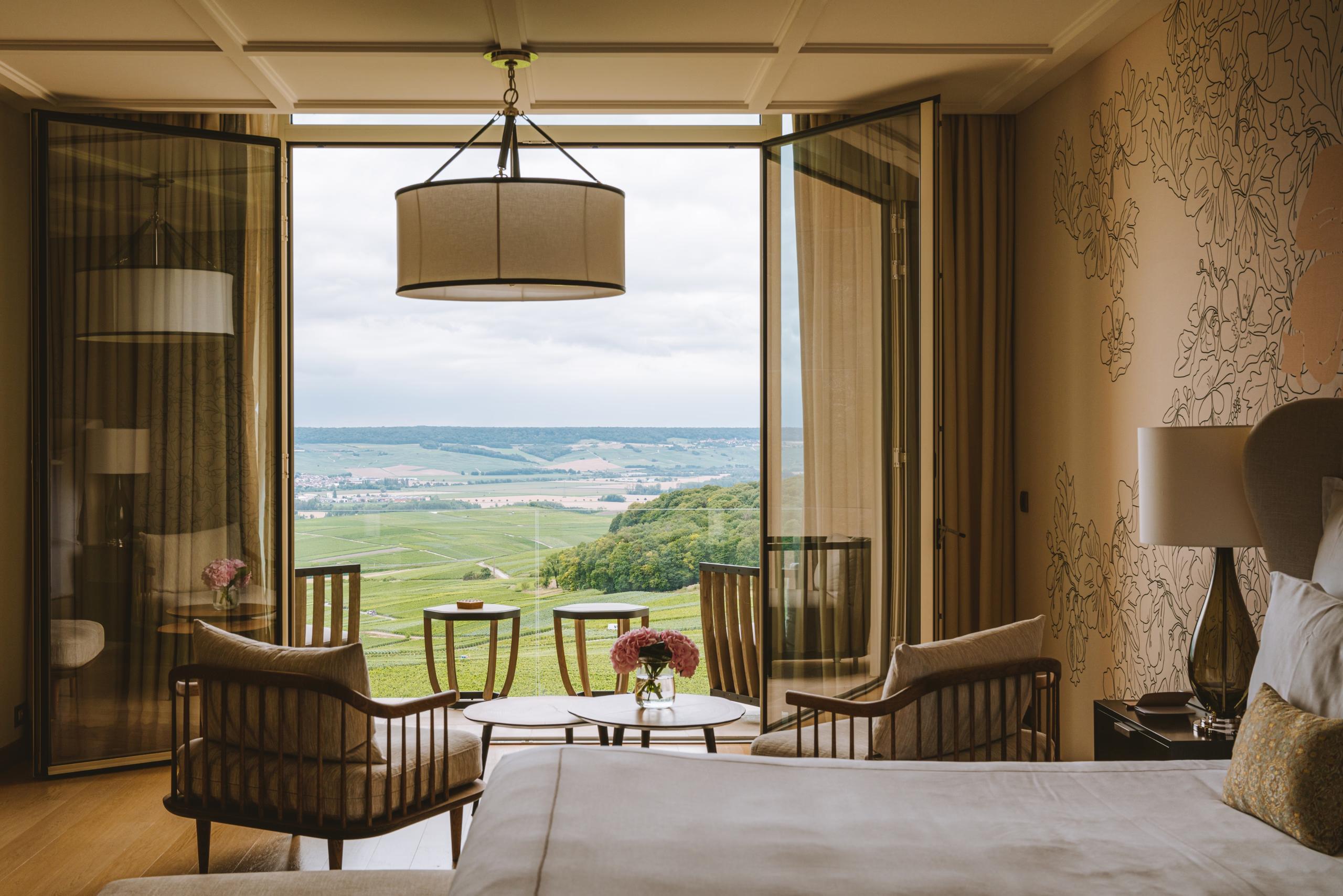 Royal Champagne Hotel & Spa: bright bedroom with soft yellow accents, large windows, and terraced seating overlooking vineyards