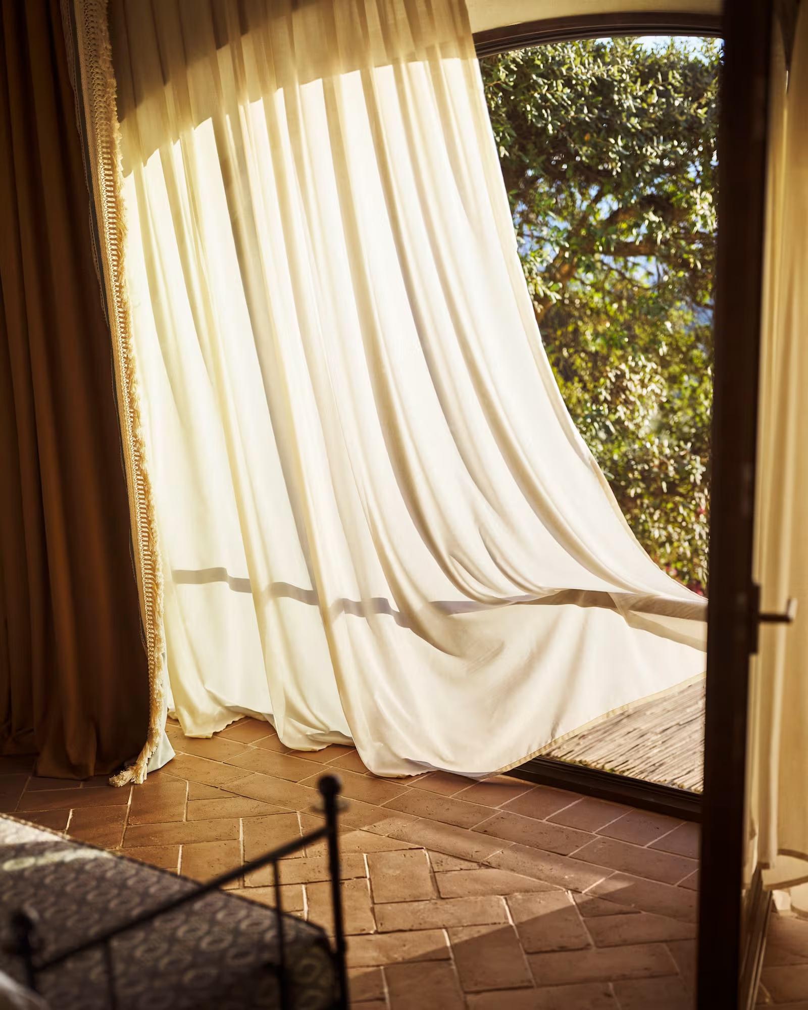 A curtain lifting at an open terrace door in the Limonaia suite, above a herringbone terracotta floor