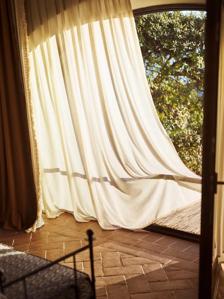 A curtain lifting at an open terrace door in the Limonaia suite, above a herringbone terracotta floor