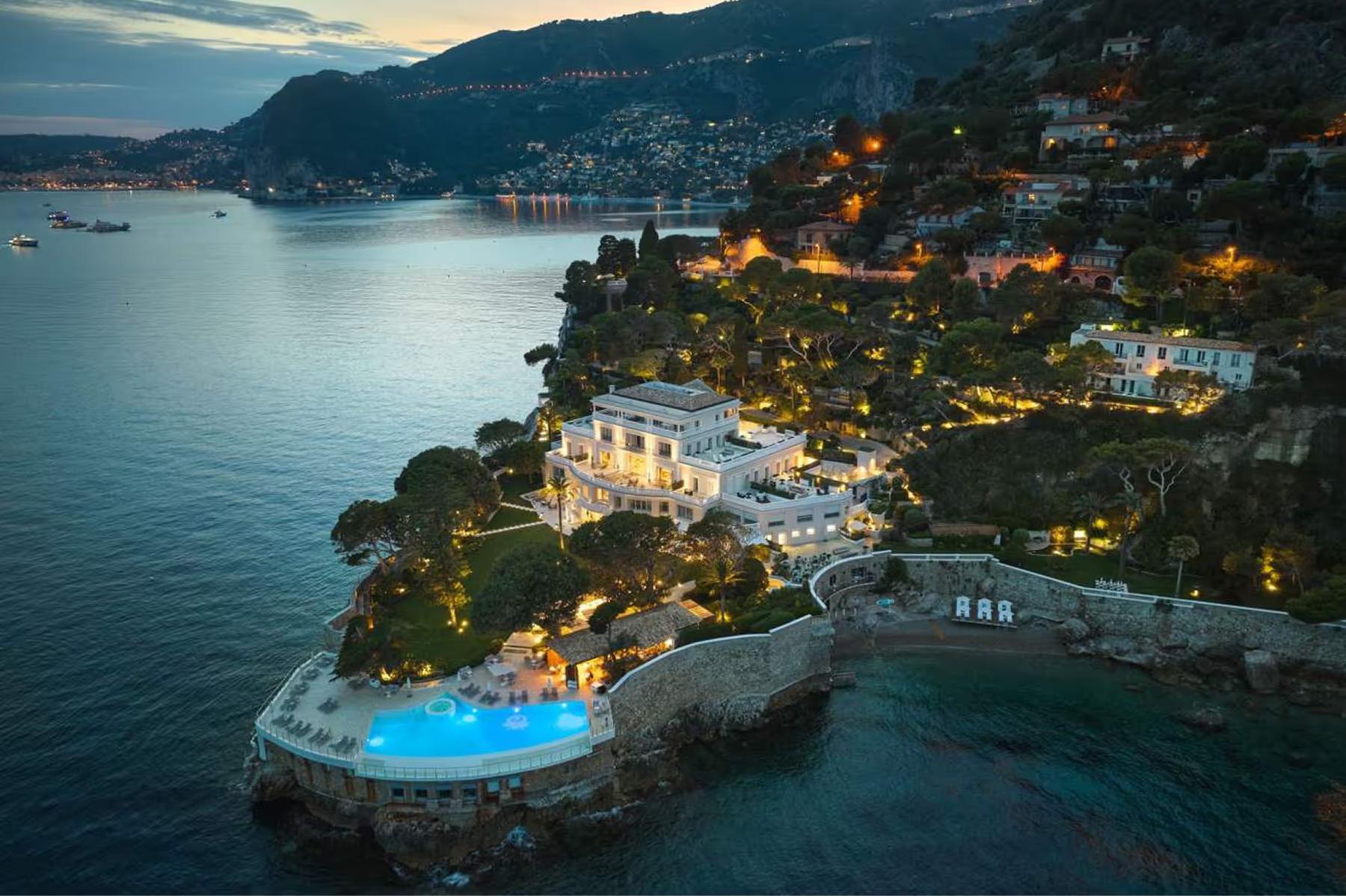 Hotel Cap-Estel: aerial dusk view of the hotel on a hillside peninsula with lit buildings