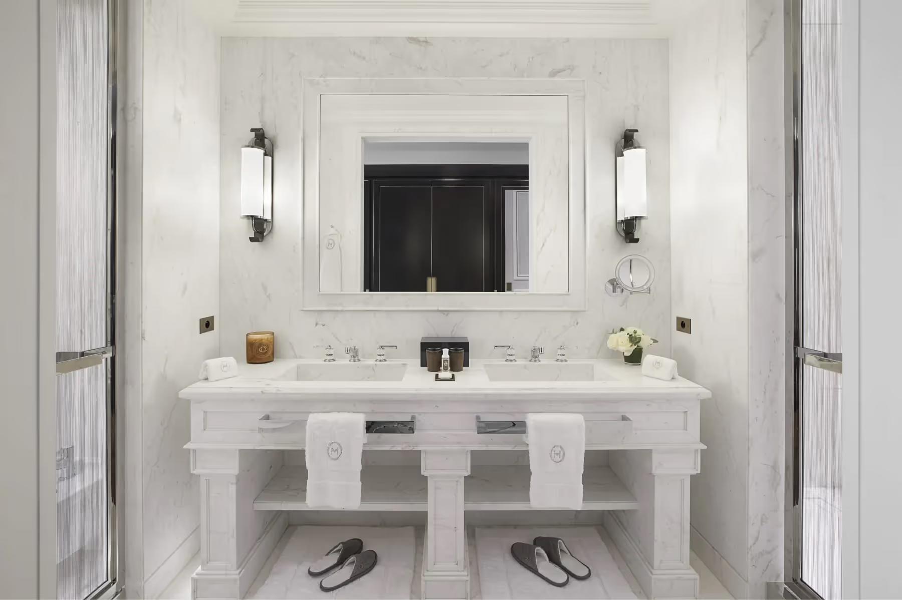 A marble bathroom with white twin vanities, large mirror, white sconces, and clean minimalist design