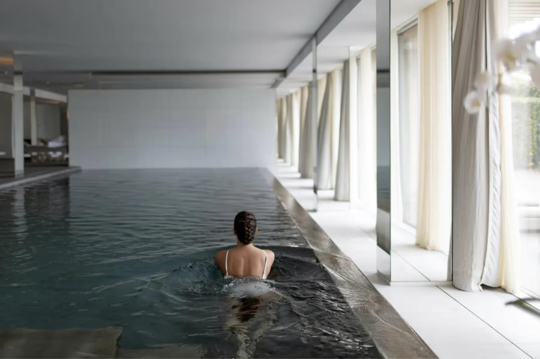 Indoor pool with person swimming in heated water and large windows