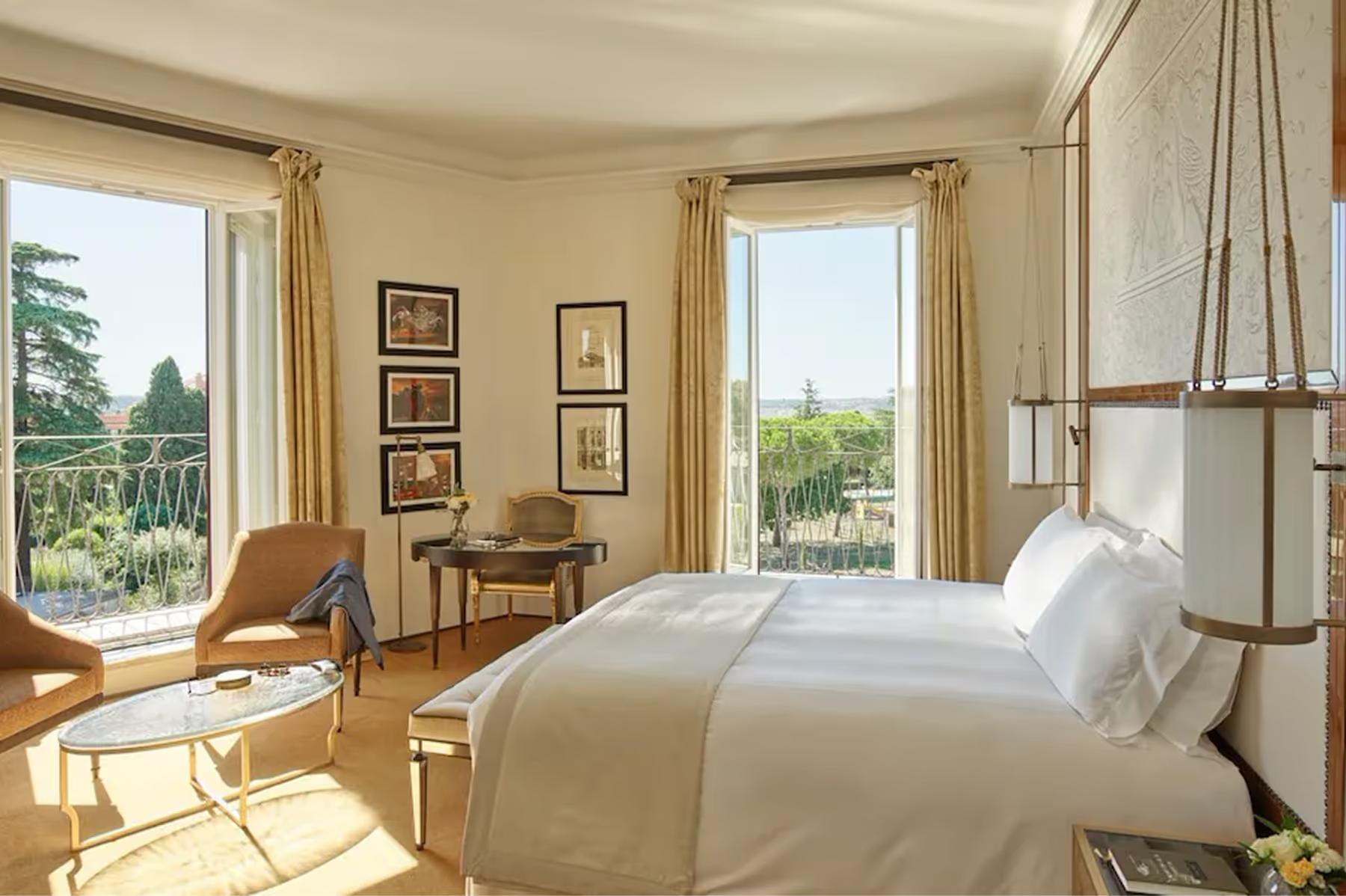 Hotel Eden: a guest room with large windows, a bed with beige linens, wooden furniture, and views of Rome’s gardens