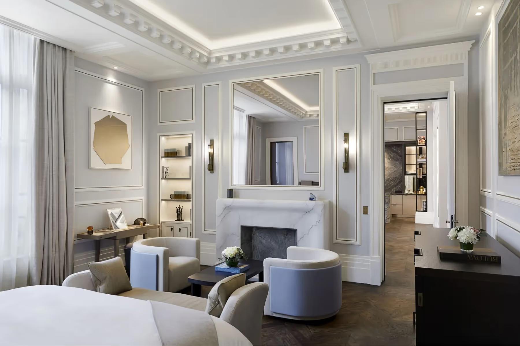 A suite with pale color palette, central fireplace, seating area, and ornate ceiling molding