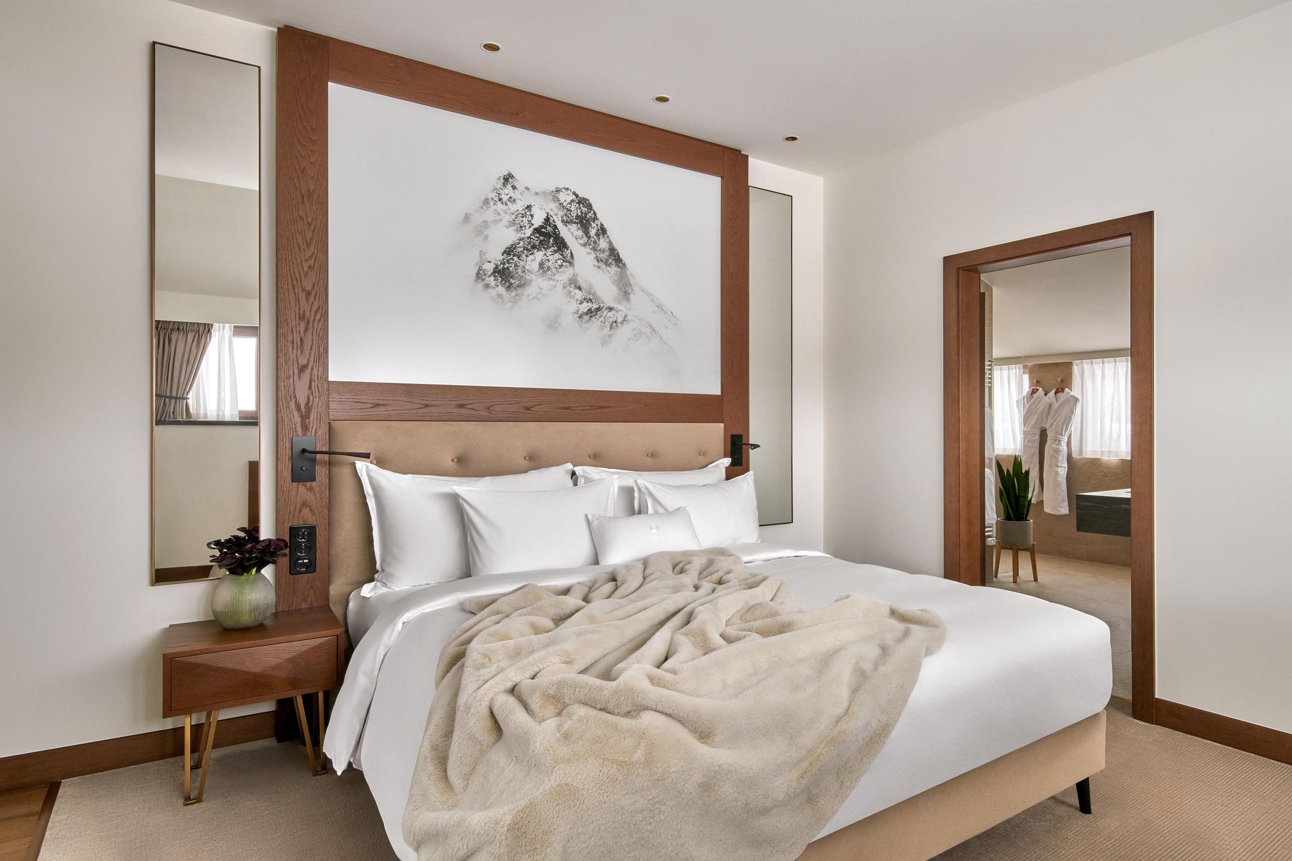 Grace La Margna St. Moritz: bedroom with wood-framed headboard, gallery art, and neutral furnishings with mountain light