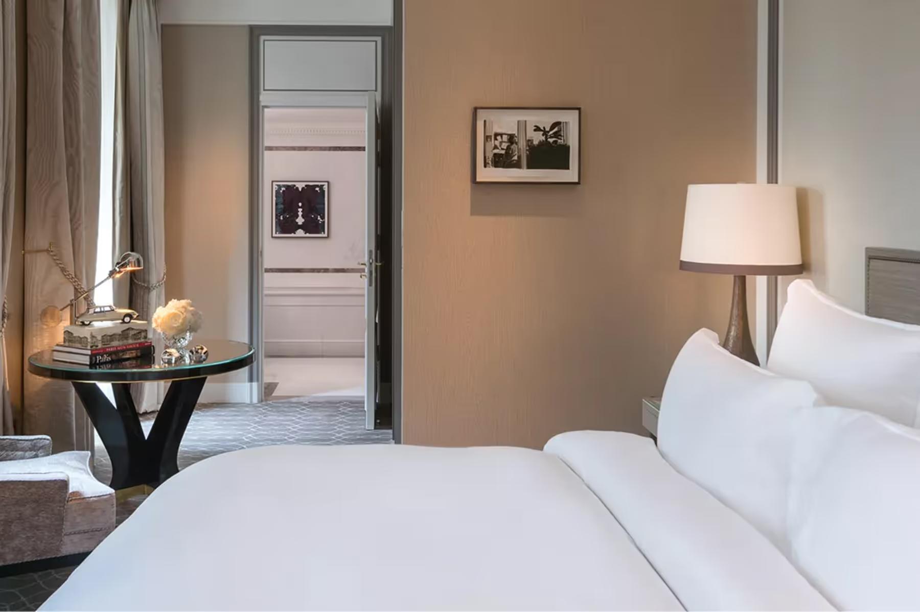 Hôtel de Crillon: neutral toned bedroom with round table, white bedding, and tan walls