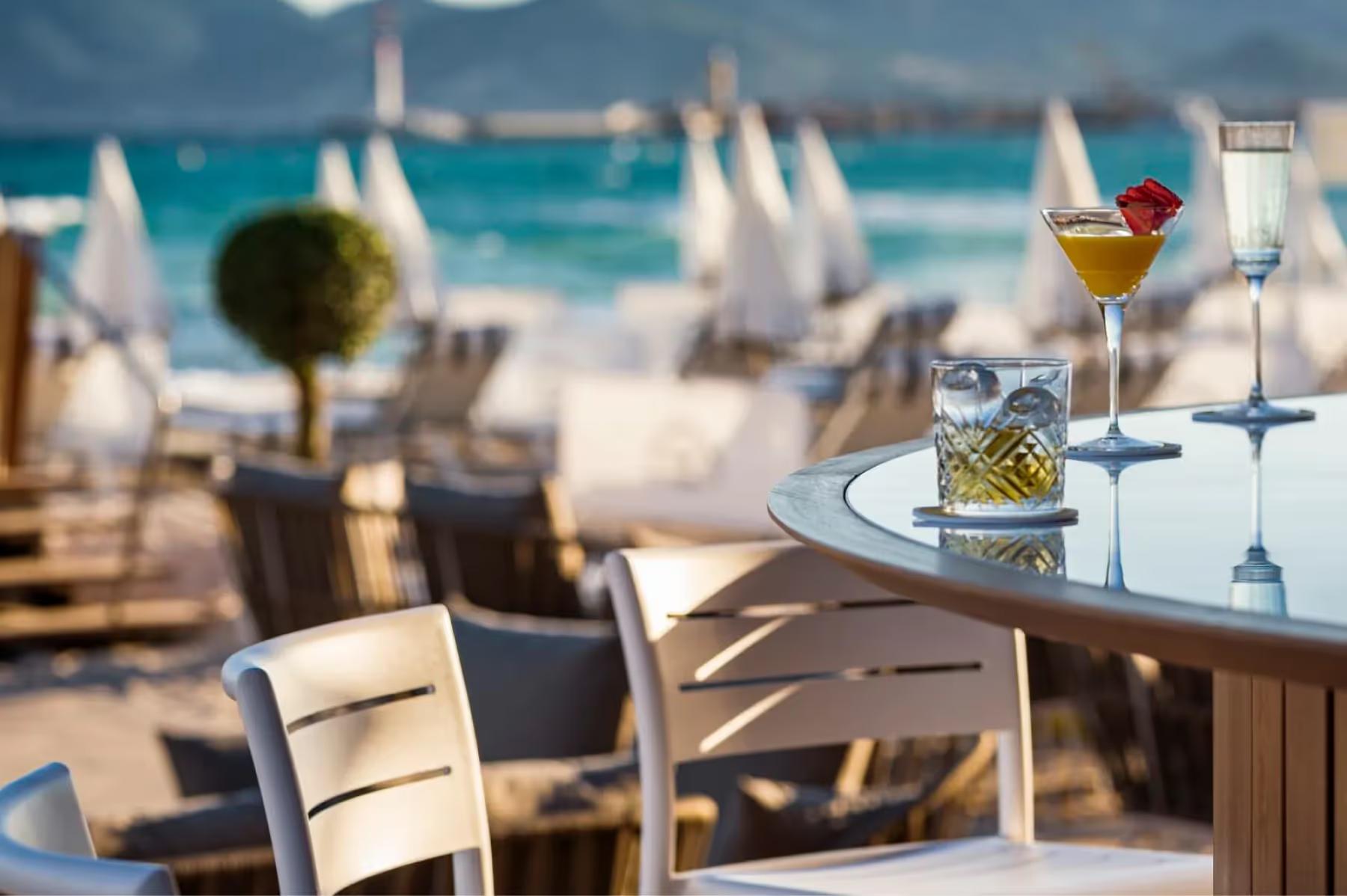 Beachfront dining with a cocktail glass and place setting in foreground overlooking the sand and sea