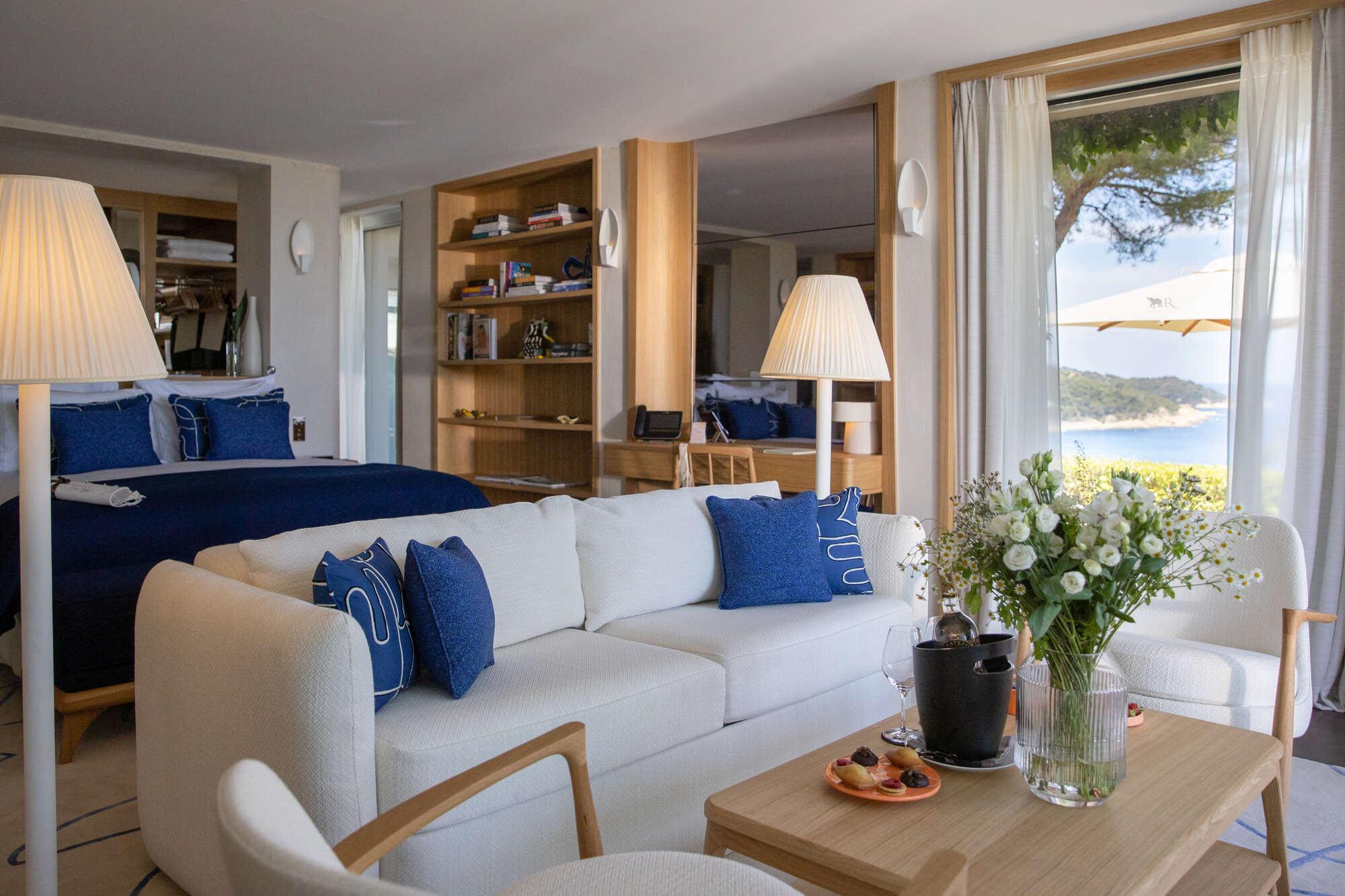 La Réserve Ramatuelle: modern suite with cream sofa and blue accents overlooking blue water