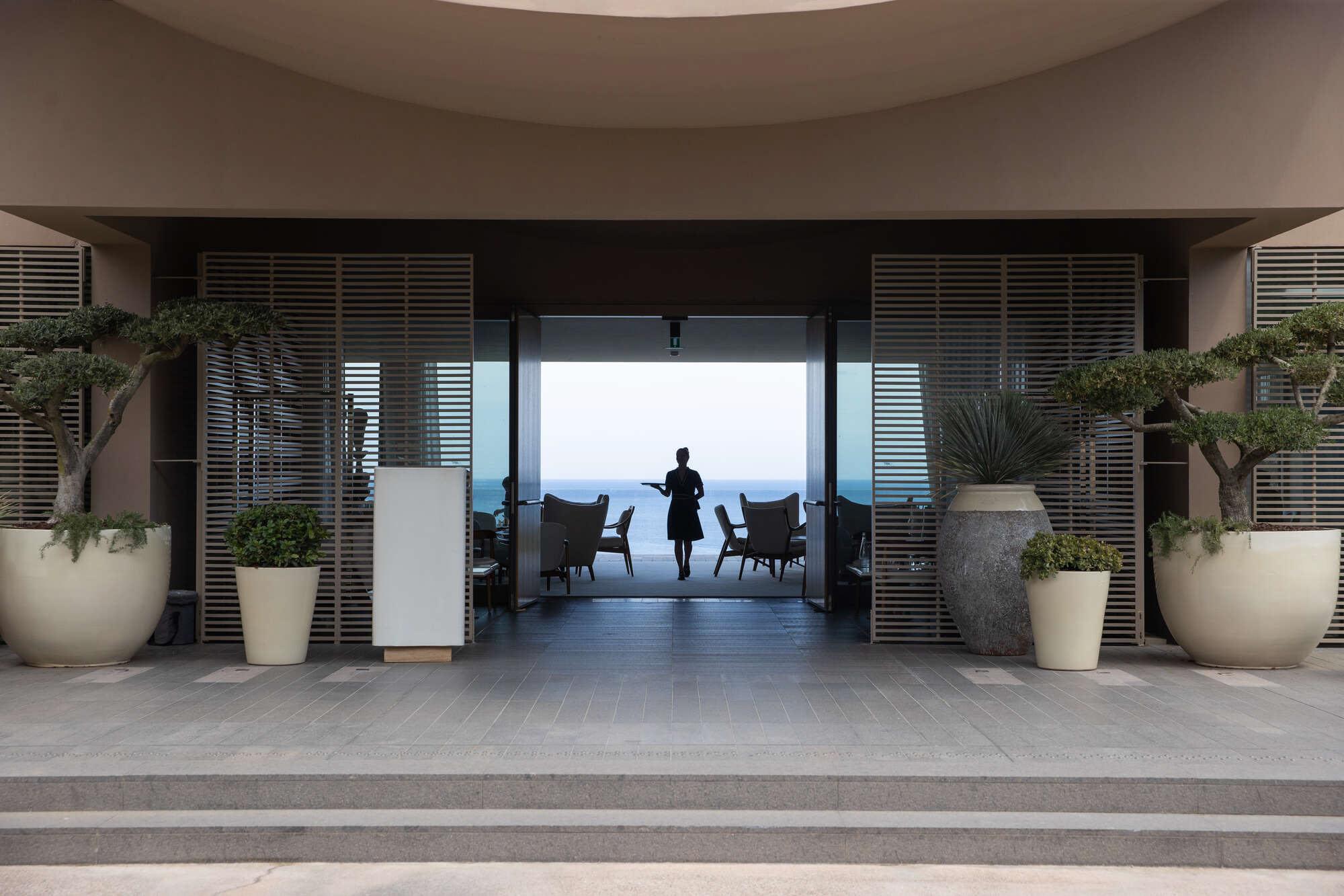 Figures walk through open doors toward a terraced seating area