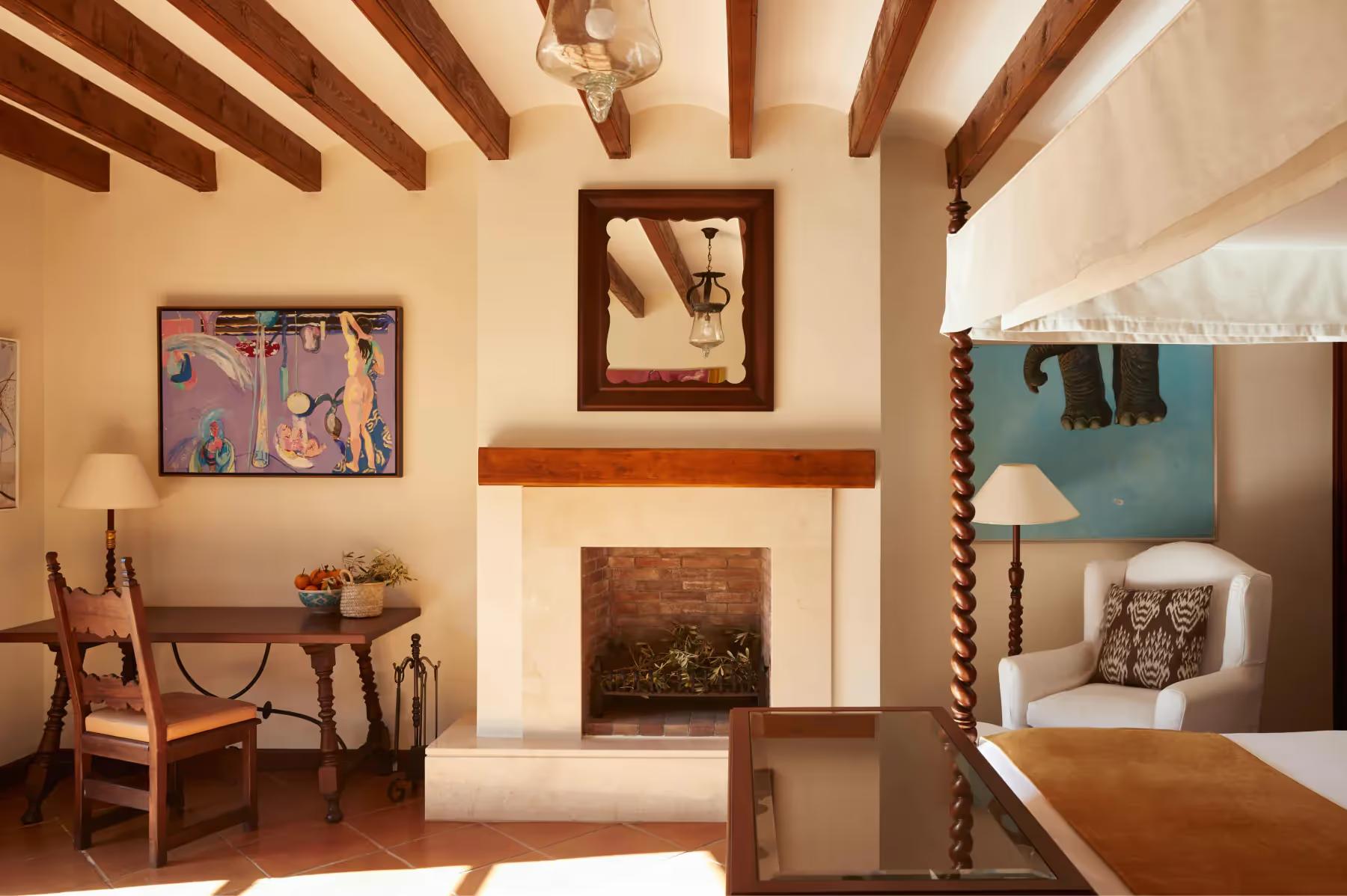La Residencia: living room with fireplace, exposed wooden beams, colorful artwork, and doorway opening to terrace